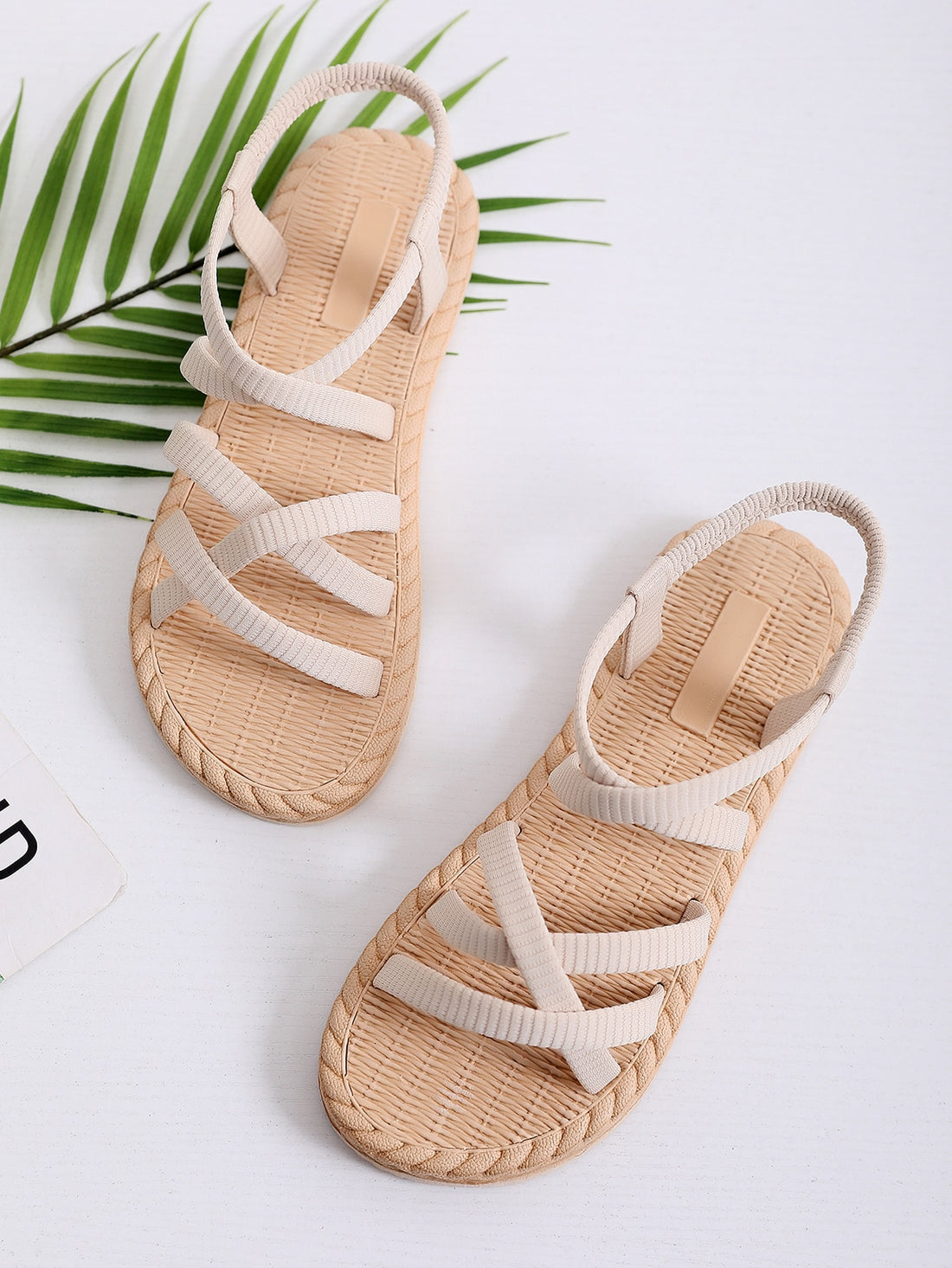 Beige women’s minimalist flat sandals with criss-cross fabric straps, open toe, and slingback design.