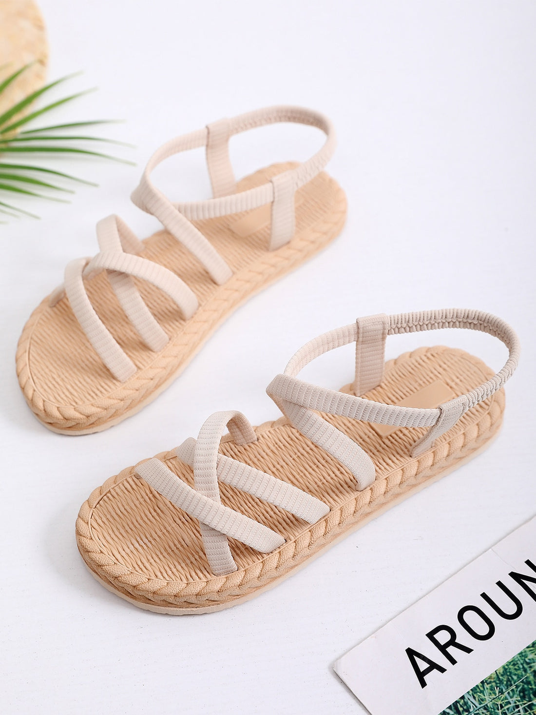 Beige women’s minimalist flat sandals with criss-cross fabric straps, open toe, and slingback design.