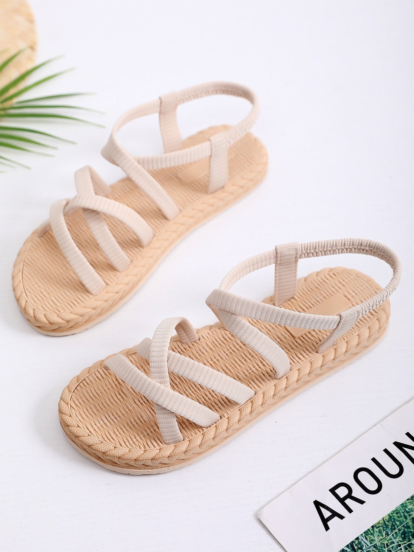 Beige women’s minimalist flat sandals with criss-cross fabric straps, open toe, and slingback design.