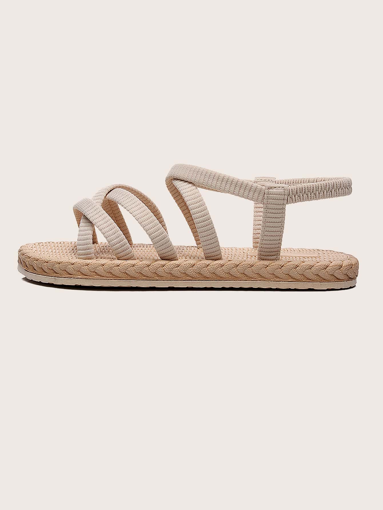Beige women’s minimalist flat sandals with criss-cross fabric straps, open toe, and slingback design.