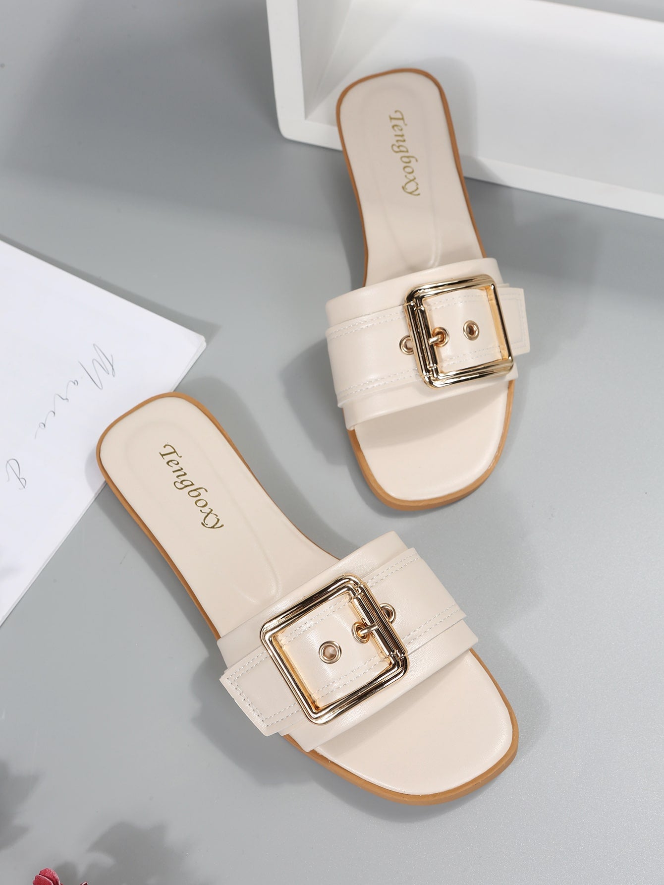 Women's beige flat slide sandals with open toe, cut-out upper, and square buckle detail, suitable for beach and summer outdoor wear.