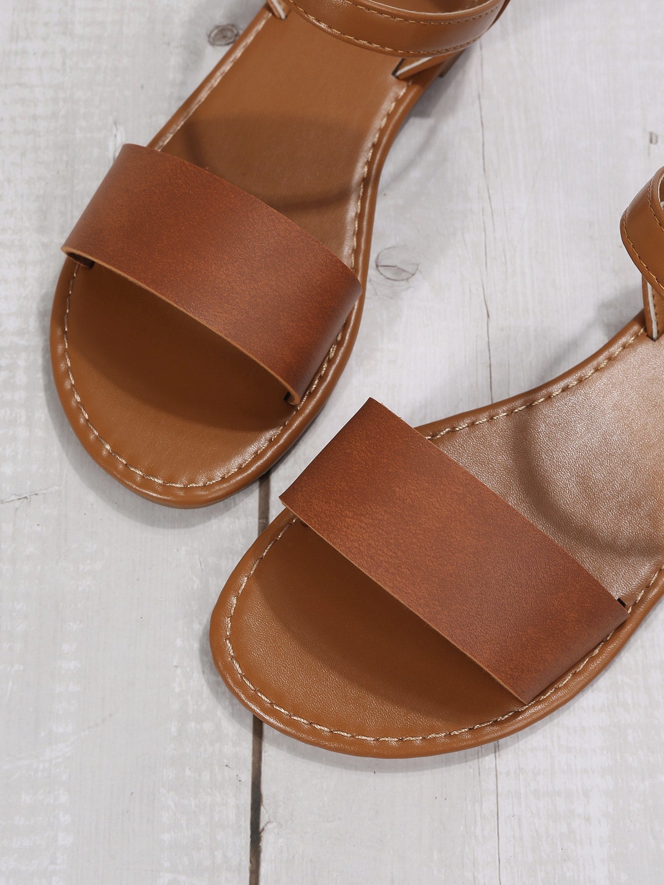 Leopard print flat sandals featuring an ankle strap with buckle detail, open toe design, and slide-style silhouette.