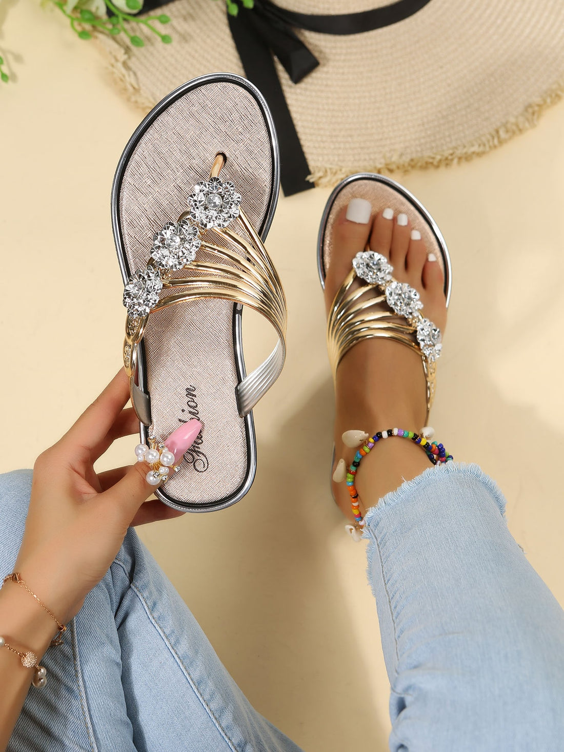 Women’s gold metallic flat thong sandals with rhinestone and flower decor, toe post design, and beach-ready style.