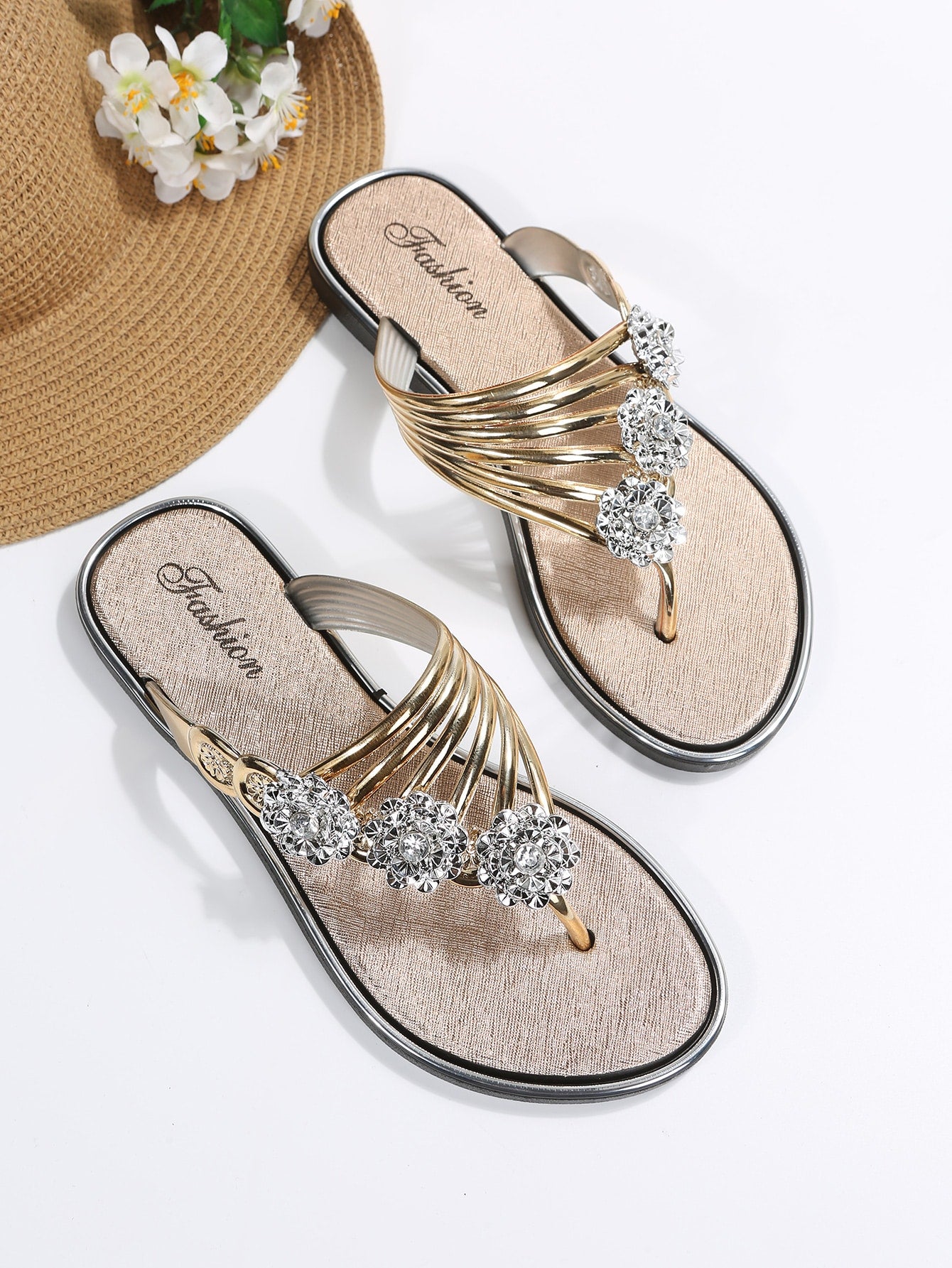 Women’s gold metallic flat thong sandals with rhinestone and flower decor, toe post design, and beach-ready style.