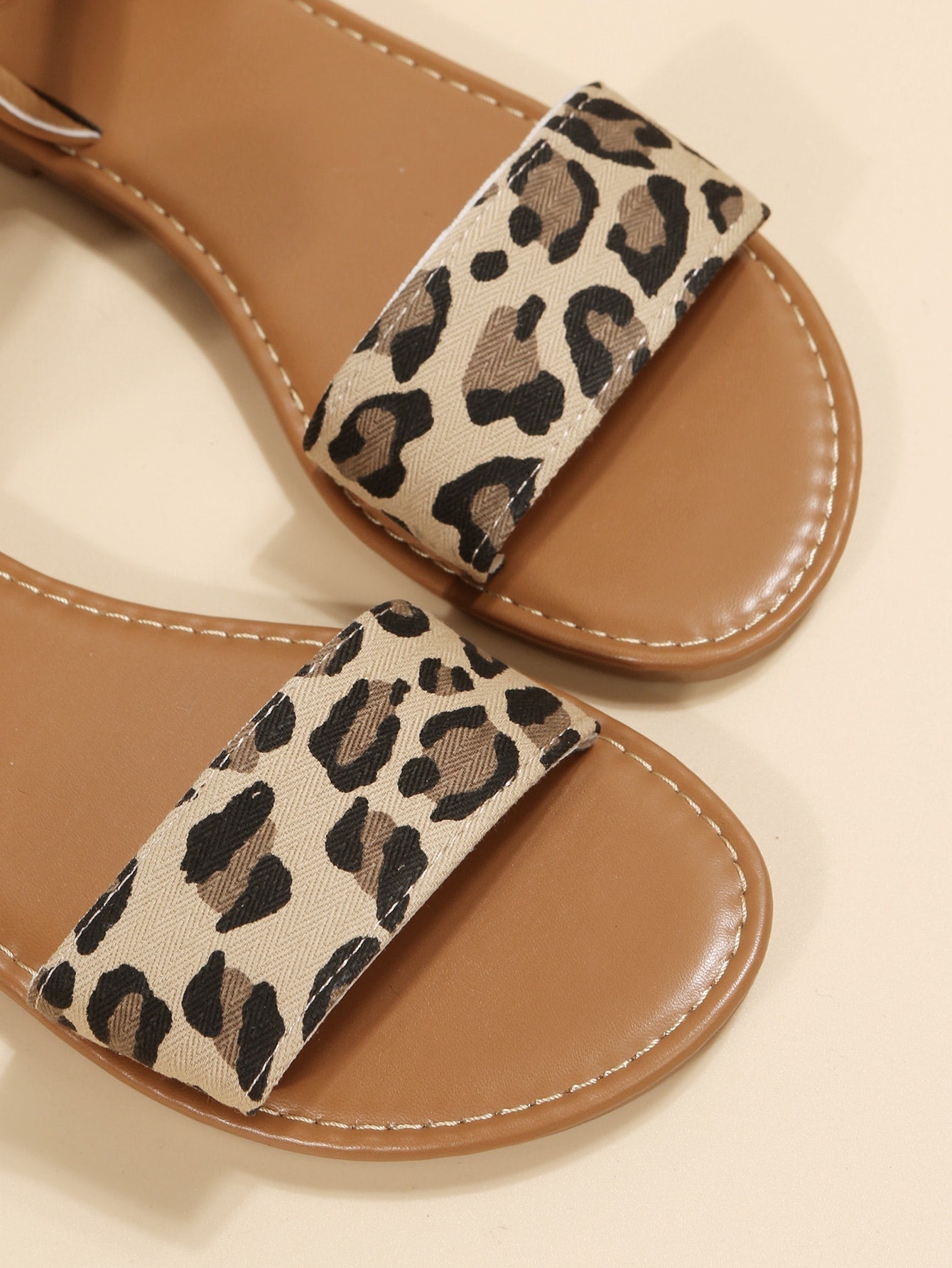 Leopard print flat sandals featuring an ankle strap with buckle detail, open toe design, and slide-style silhouette.