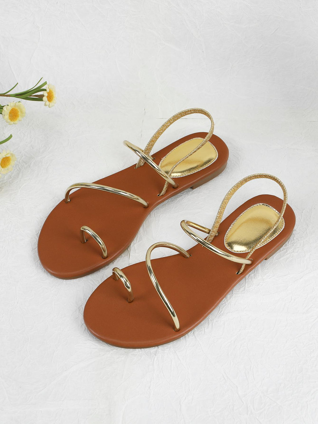 Pair of women’s gold flat sandals featuring a toe ring thong toe post design, criss-cross straps, and a slingback ankle strap.