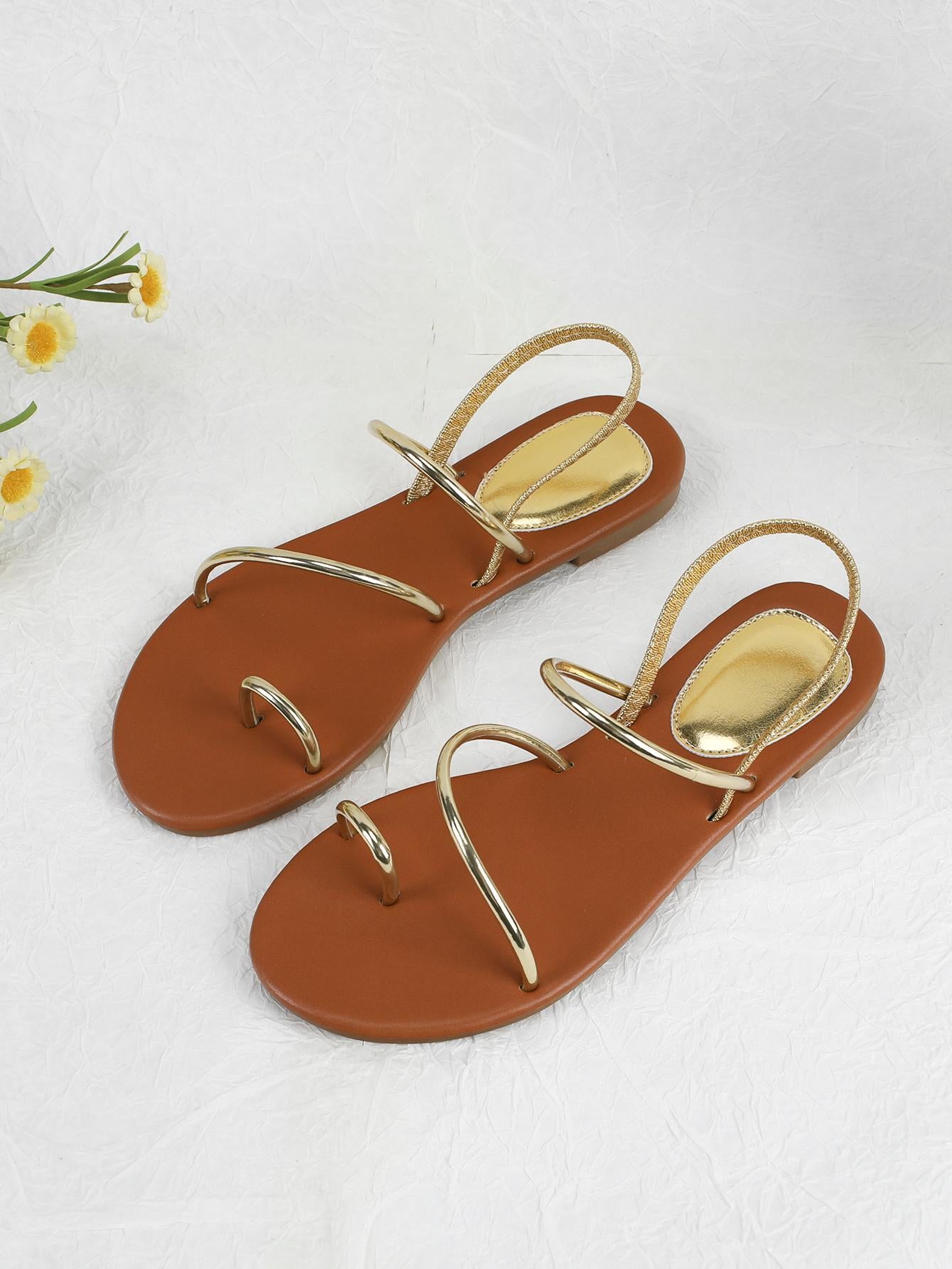 Pair of women’s gold flat sandals featuring a toe ring thong toe post design, criss-cross straps, and a slingback ankle strap.