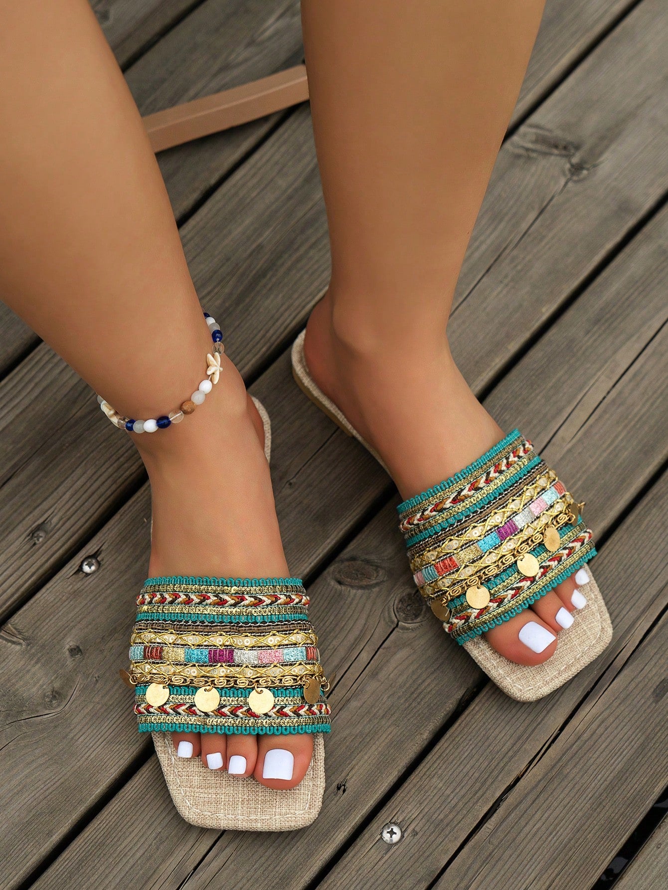 Pair of green women’s flat slide sandals with open toes, embroidered and beaded detailing, and fringe accents in a vacation style.
