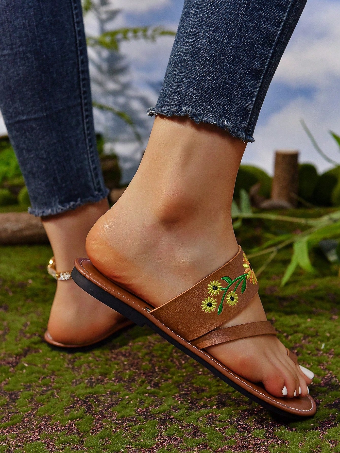 Women's mocha brown flat toe-post flip flops with sunflower design, woven slingback strap, and buckle chain detail, styled as comfortable beach sandals.