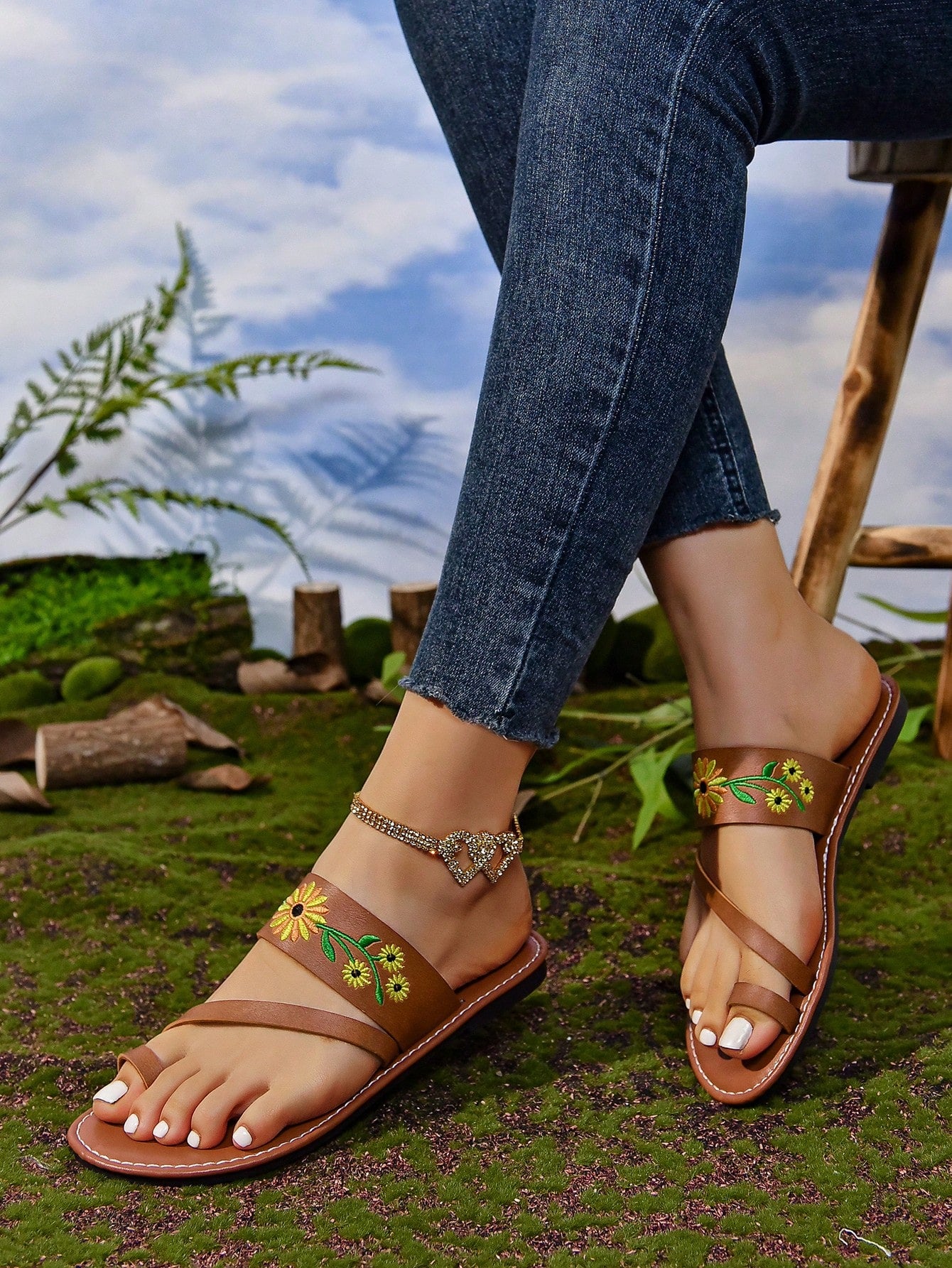 Women's mocha brown flat toe-post flip flops with sunflower design, woven slingback strap, and buckle chain detail, styled as comfortable beach sandals.