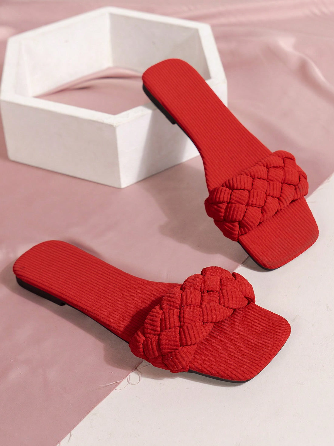 Women's red flat slide sandals with an open toe, woven one-strap upper, and metal buckle detail.