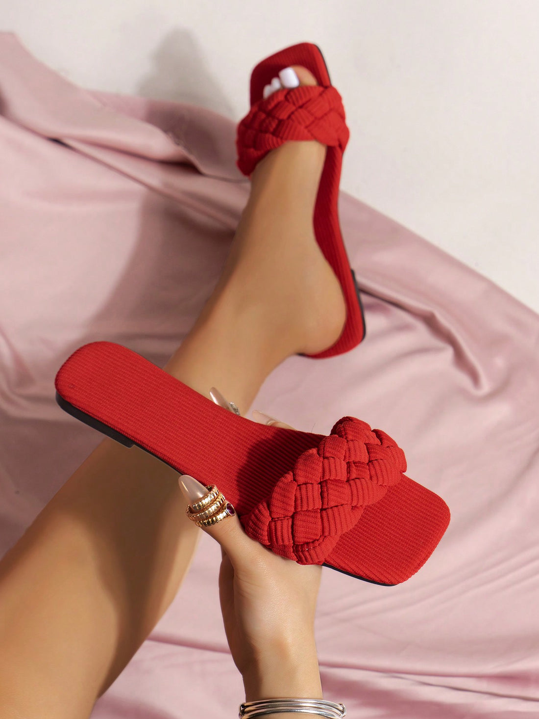 Women's red flat slide sandals with an open toe, woven one-strap upper, and metal buckle detail.
