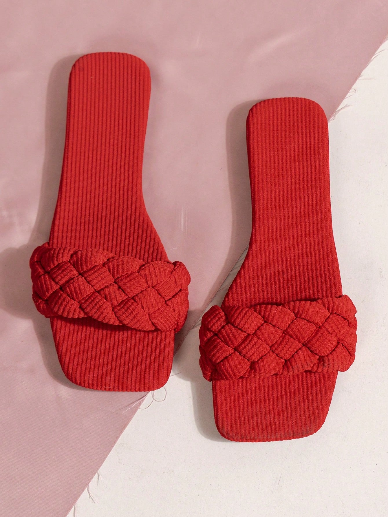 Women's red flat slide sandals with an open toe, woven one-strap upper, and metal buckle detail.