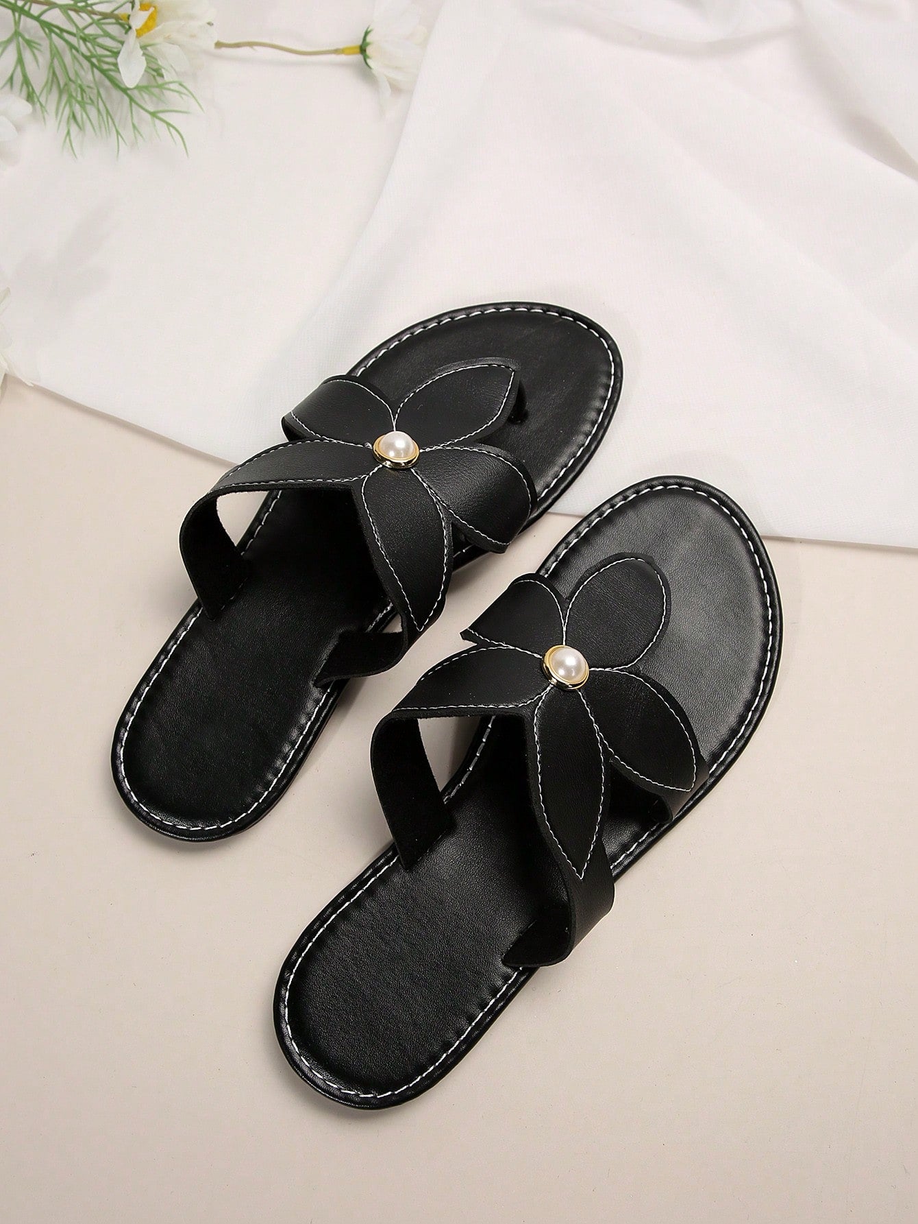 Pair of women’s black floral flat slide sandals with open toe and toe-post design, featuring pearl details and a casual summer beach style.