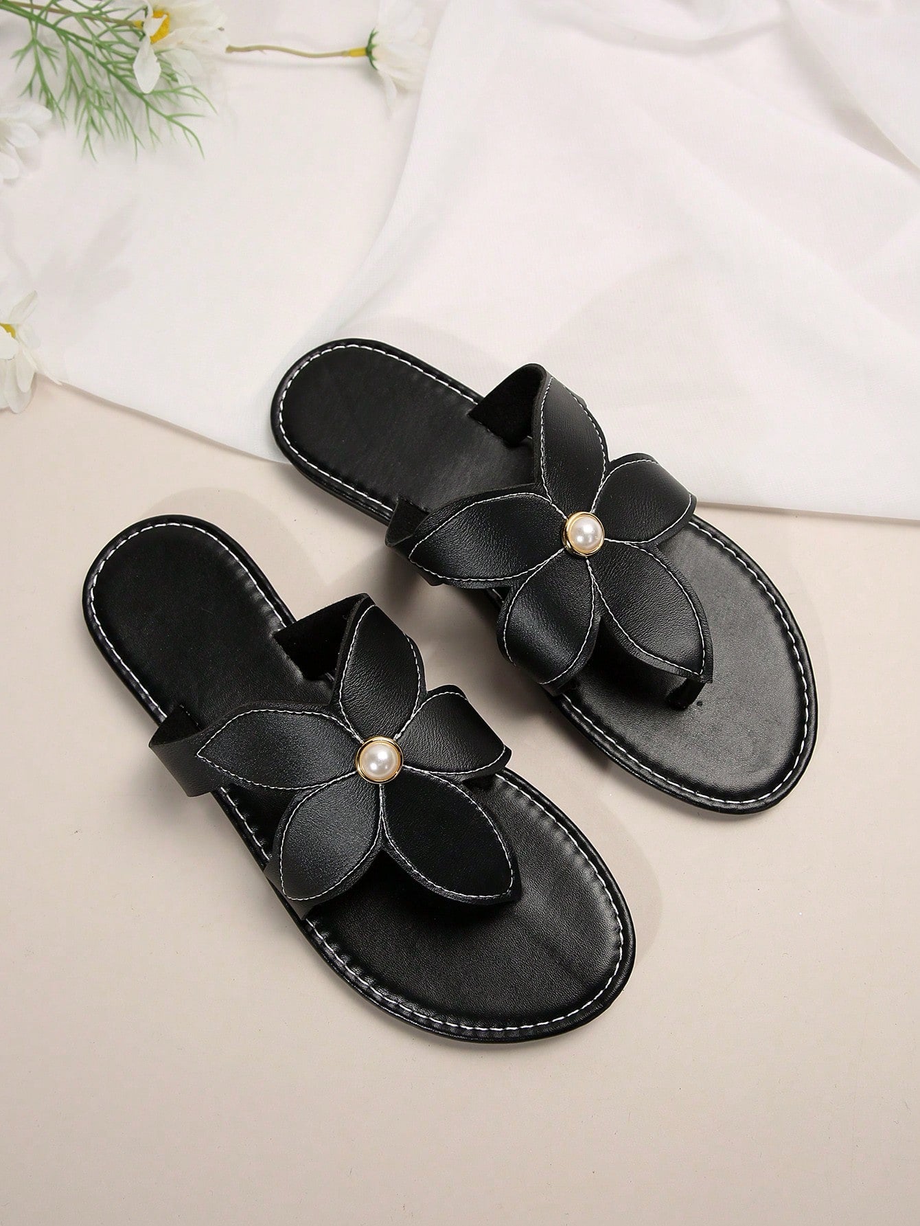 Pair of women’s black floral flat slide sandals with open toe and toe-post design, featuring pearl details and a casual summer beach style.
