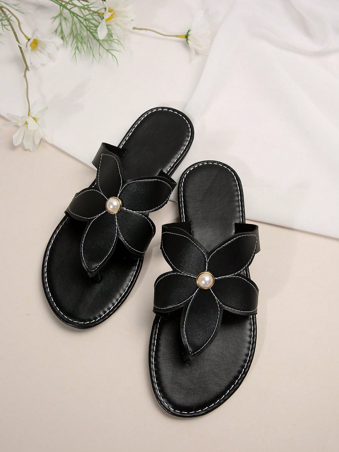 Pair of women’s black floral flat slide sandals with open toe and toe-post design, featuring pearl details and a casual summer beach style.