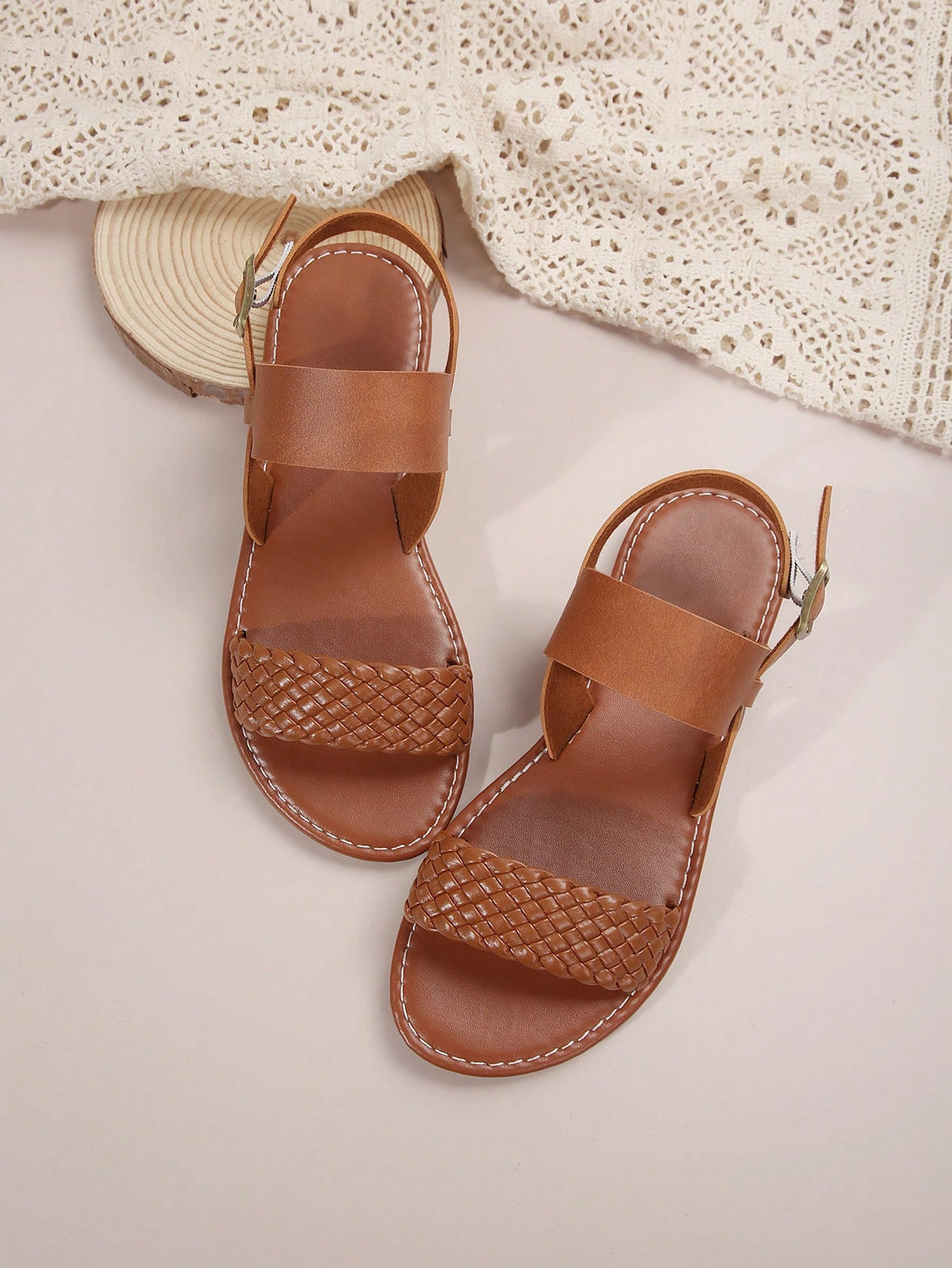 Pair of women’s coffee brown flat sandals with woven braid straps, open toe design, and buckle closure, suitable for casual beach outfits.