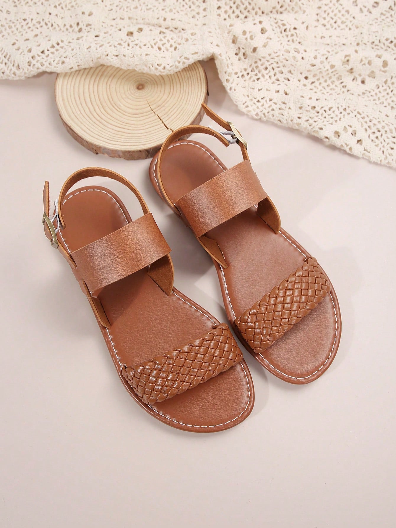 Pair of women’s coffee brown flat sandals with woven braid straps, open toe design, and buckle closure, suitable for casual beach outfits.