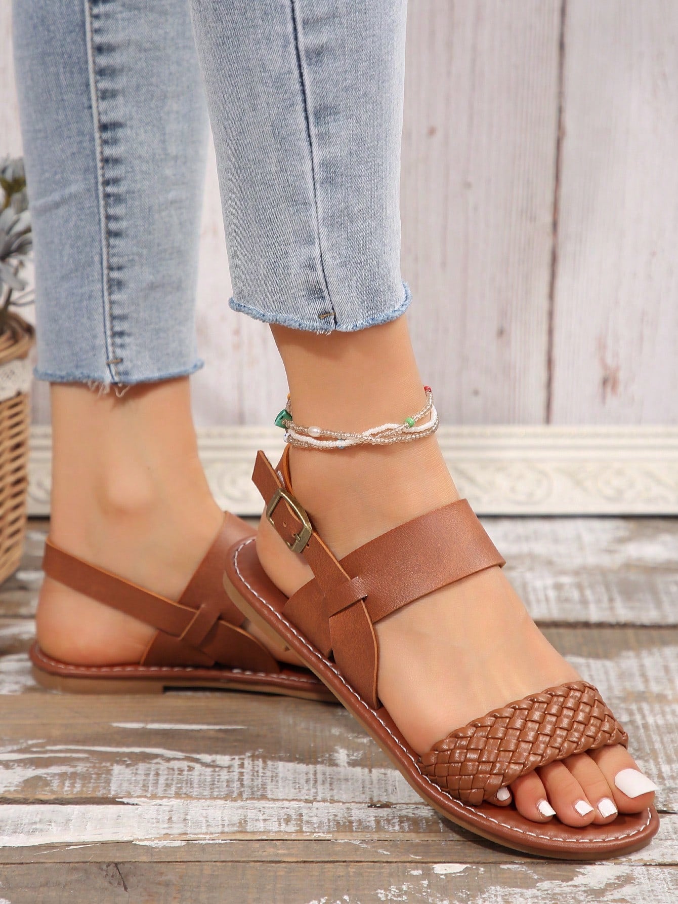 Pair of women’s coffee brown flat sandals with woven braid straps, open toe design, and buckle closure, suitable for casual beach outfits.
