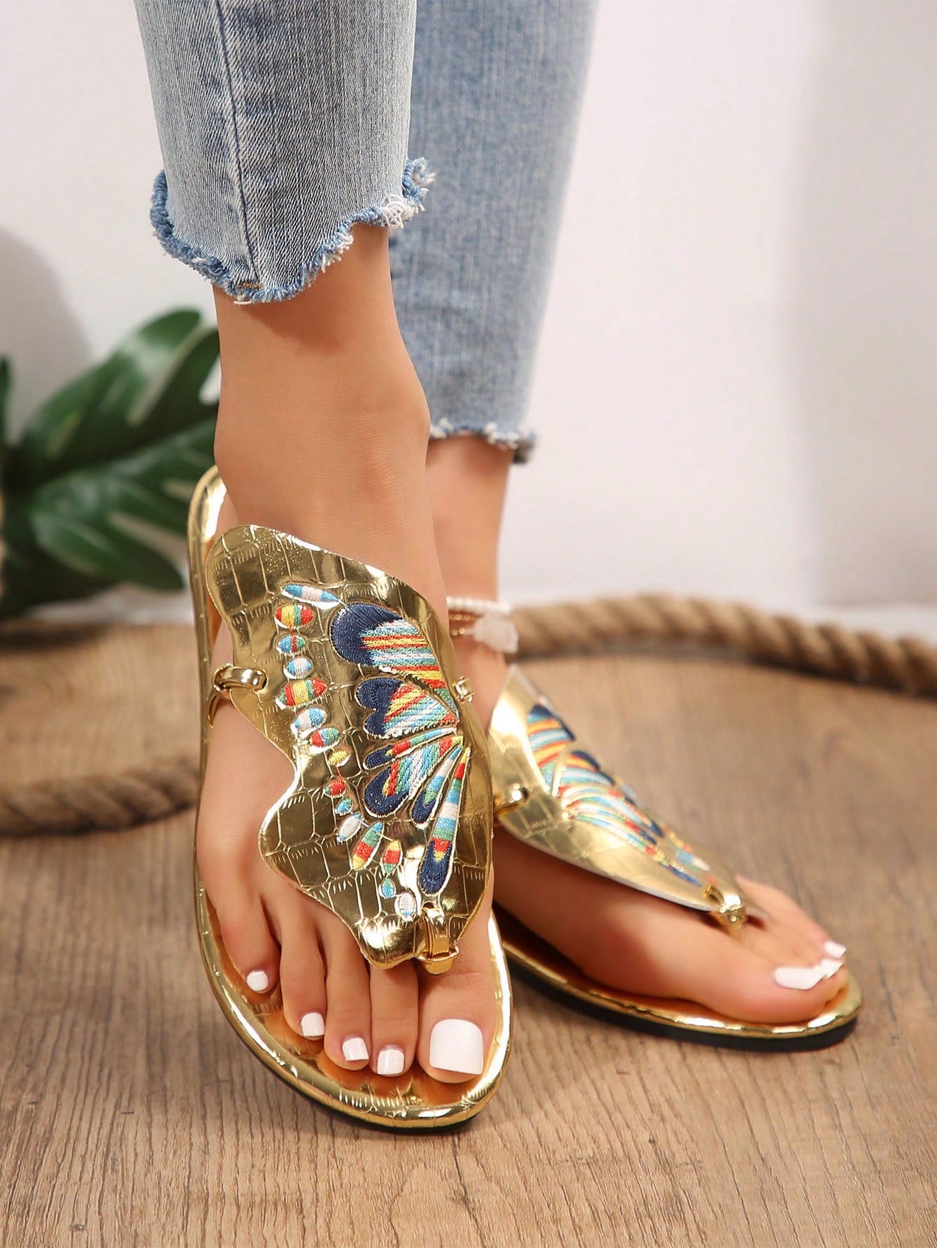 Pair of women’s gold flat slide sandals with butterfly embroidery, shiny retro-inspired look, and toe post design.