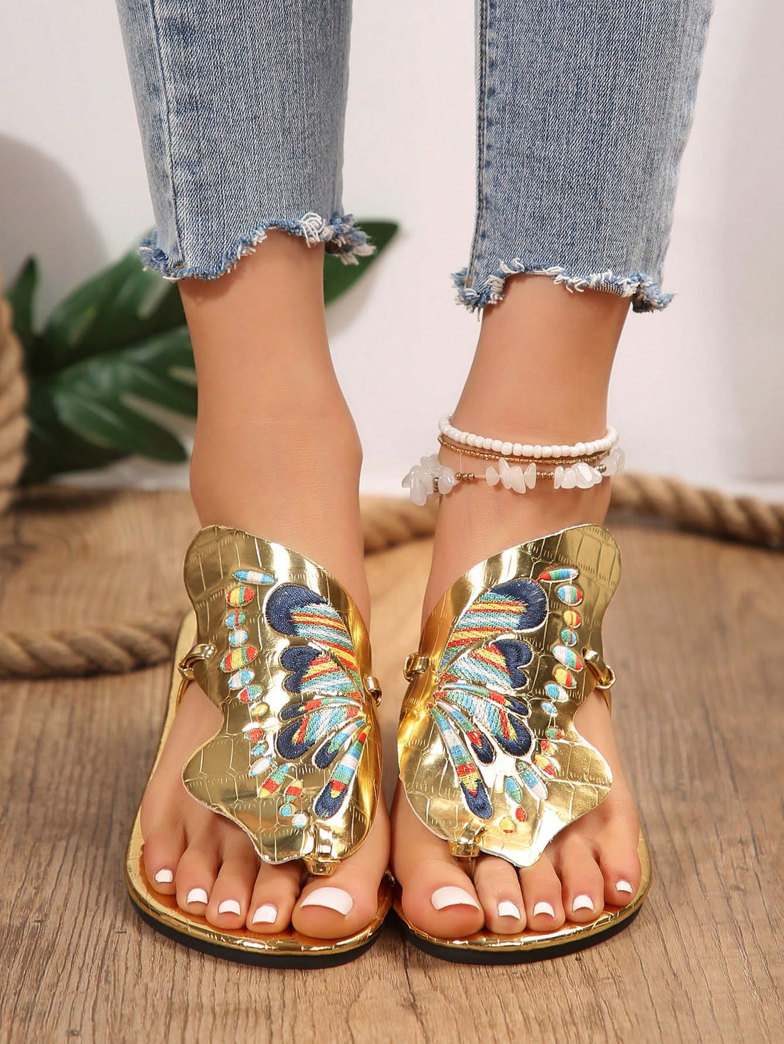 Pair of women’s gold flat slide sandals with butterfly embroidery, shiny retro-inspired look, and toe post design.