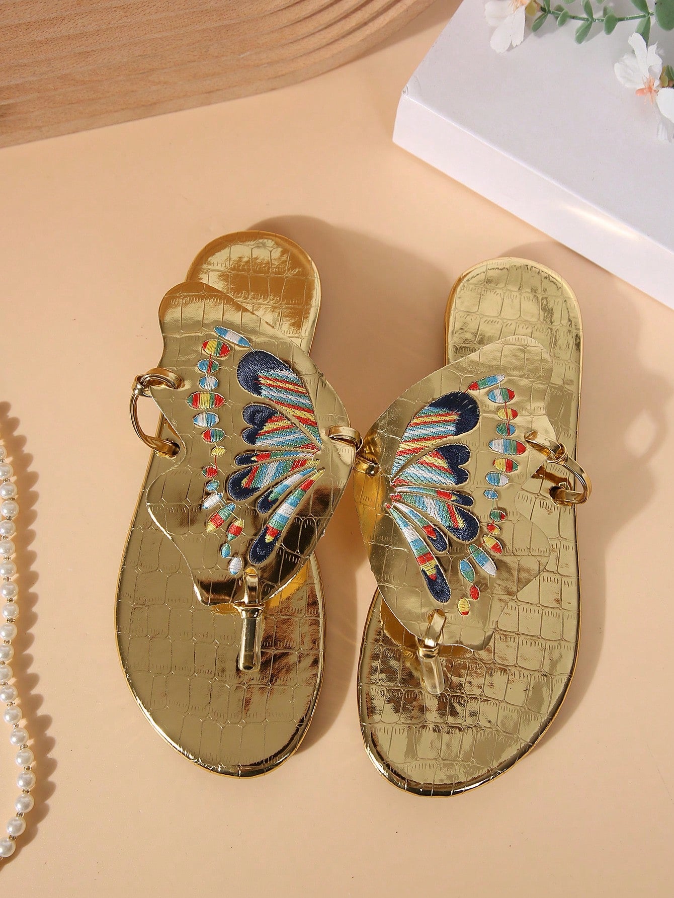 Pair of women’s gold flat slide sandals with butterfly embroidery, shiny retro-inspired look, and toe post design.
