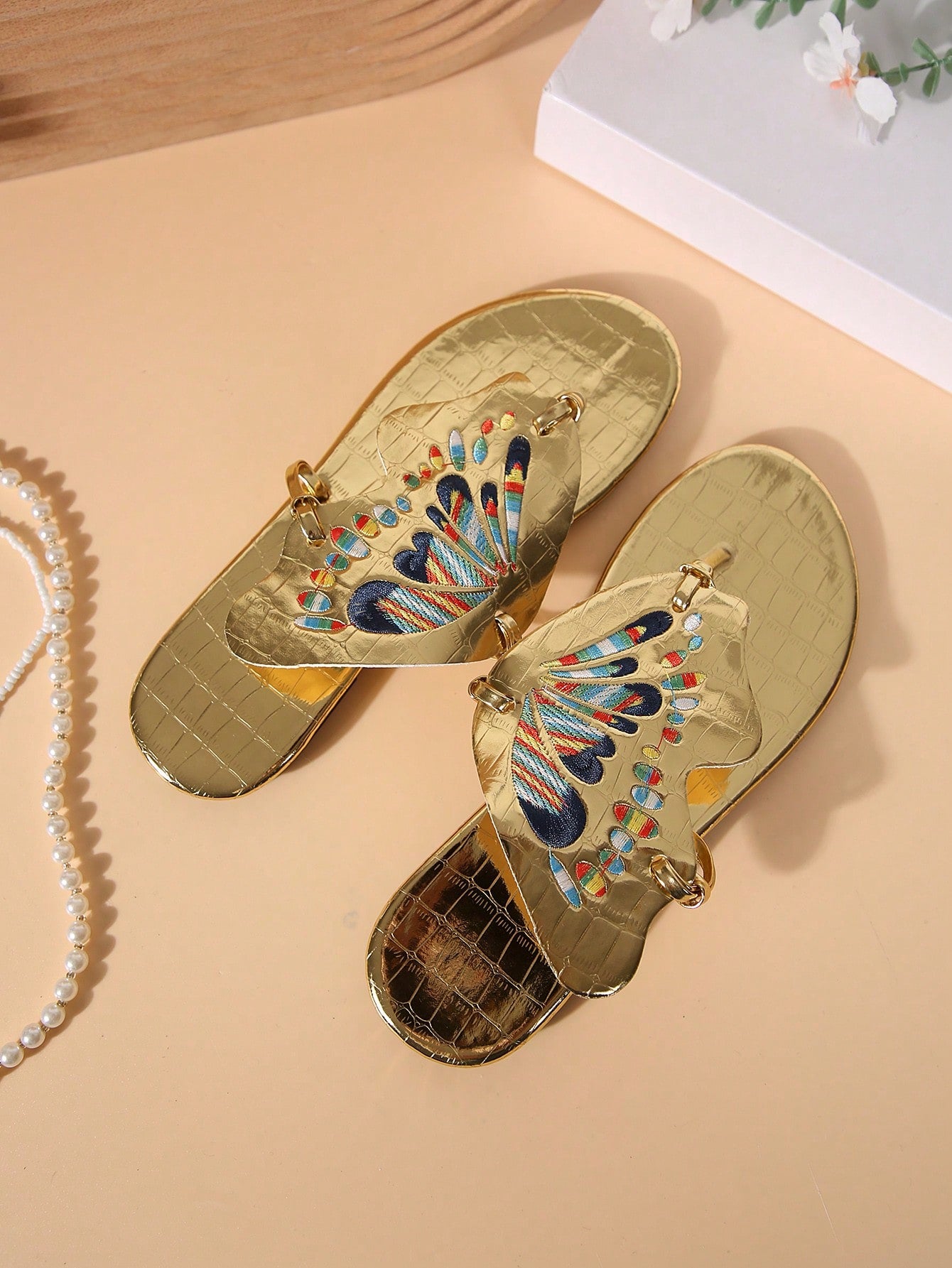 Pair of women’s gold flat slide sandals with butterfly embroidery, shiny retro-inspired look, and toe post design.