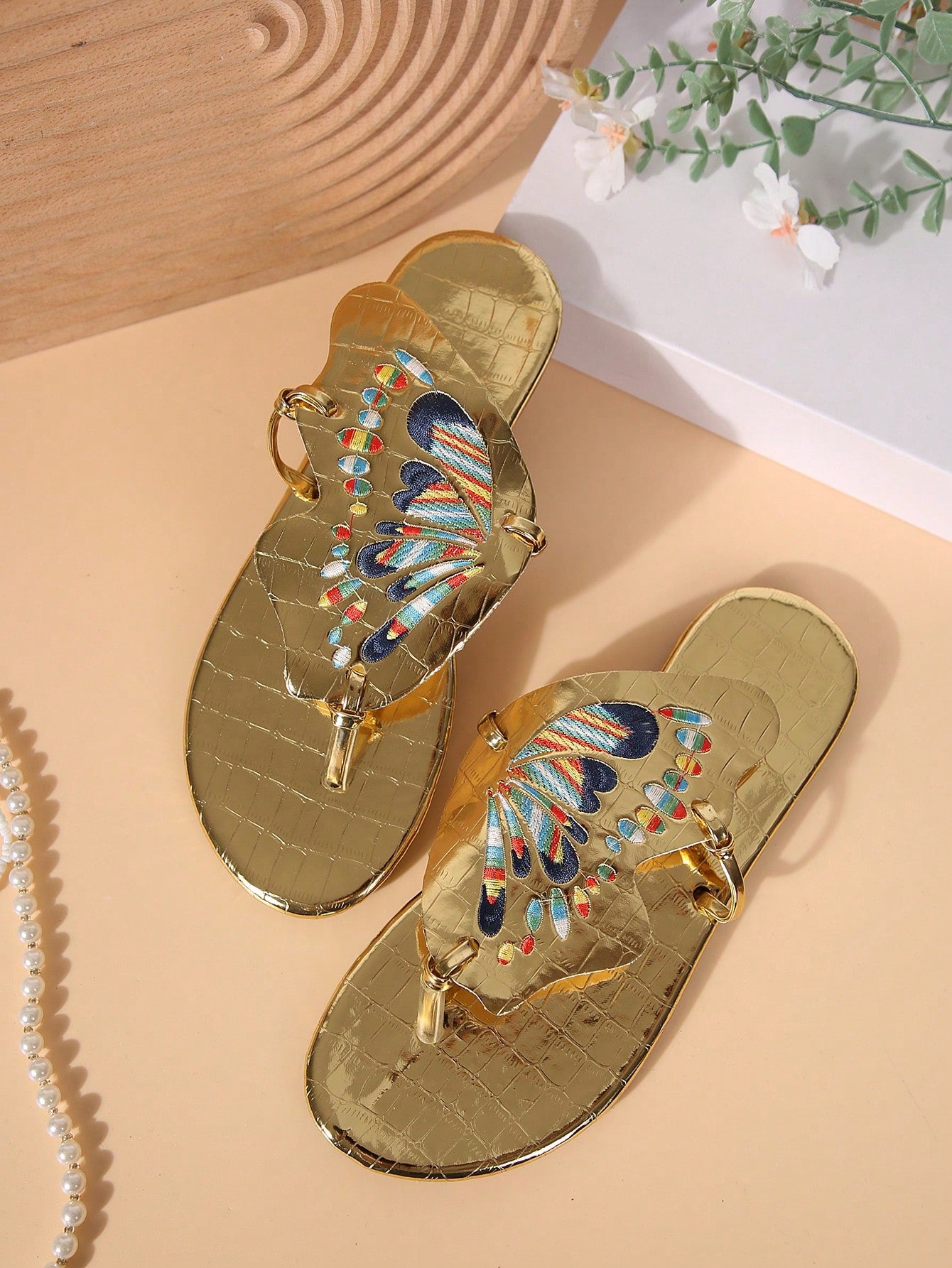 Pair of women’s gold flat slide sandals with butterfly embroidery, shiny retro-inspired look, and toe post design.