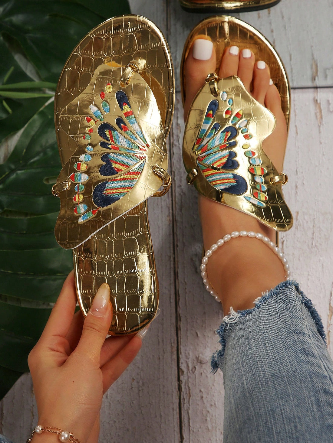 Pair of women’s gold flat slide sandals with butterfly embroidery, shiny retro-inspired look, and toe post design.