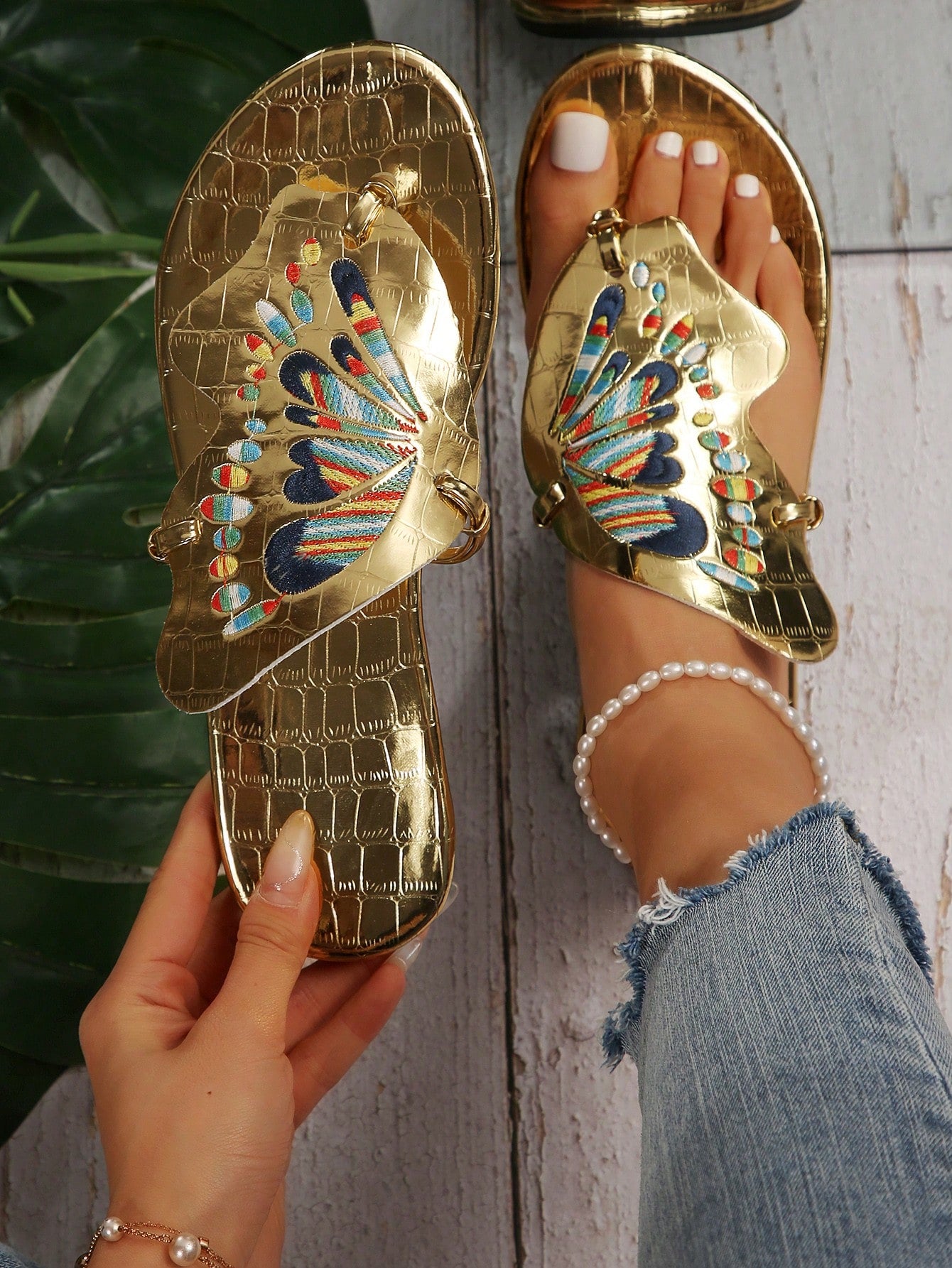 Pair of women’s gold flat slide sandals with butterfly embroidery, shiny retro-inspired look, and toe post design.