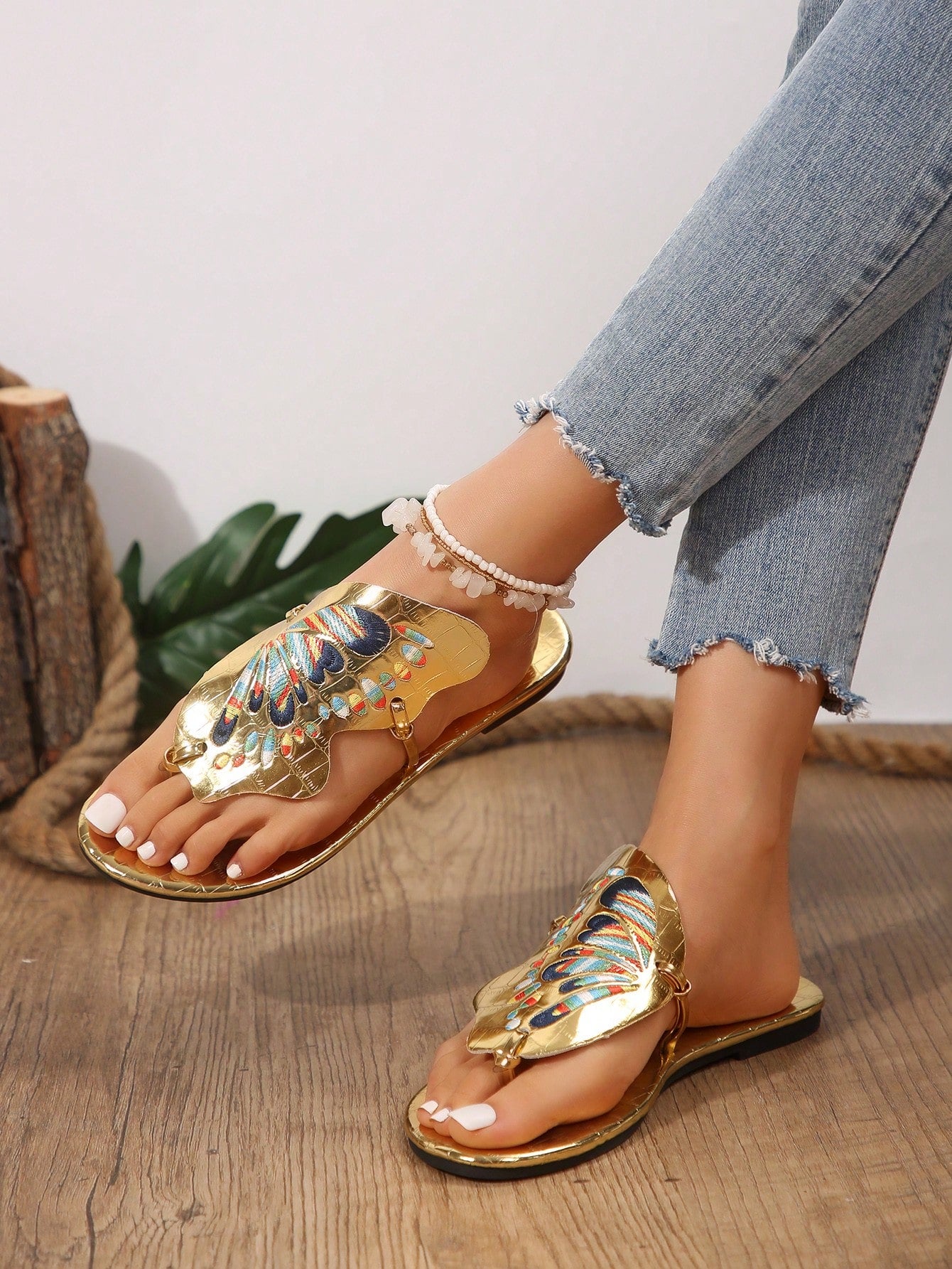 Pair of women’s gold flat slide sandals with butterfly embroidery, shiny retro-inspired look, and toe post design.