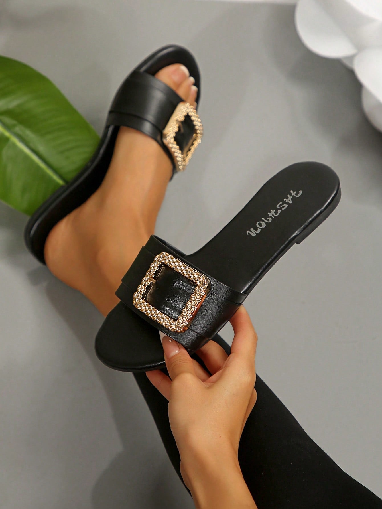Pair of women's black flat slide sandals featuring rhinestone embellishments, metal accents, and a gold-strip detail on the upper, with an open-toe slip-on design.