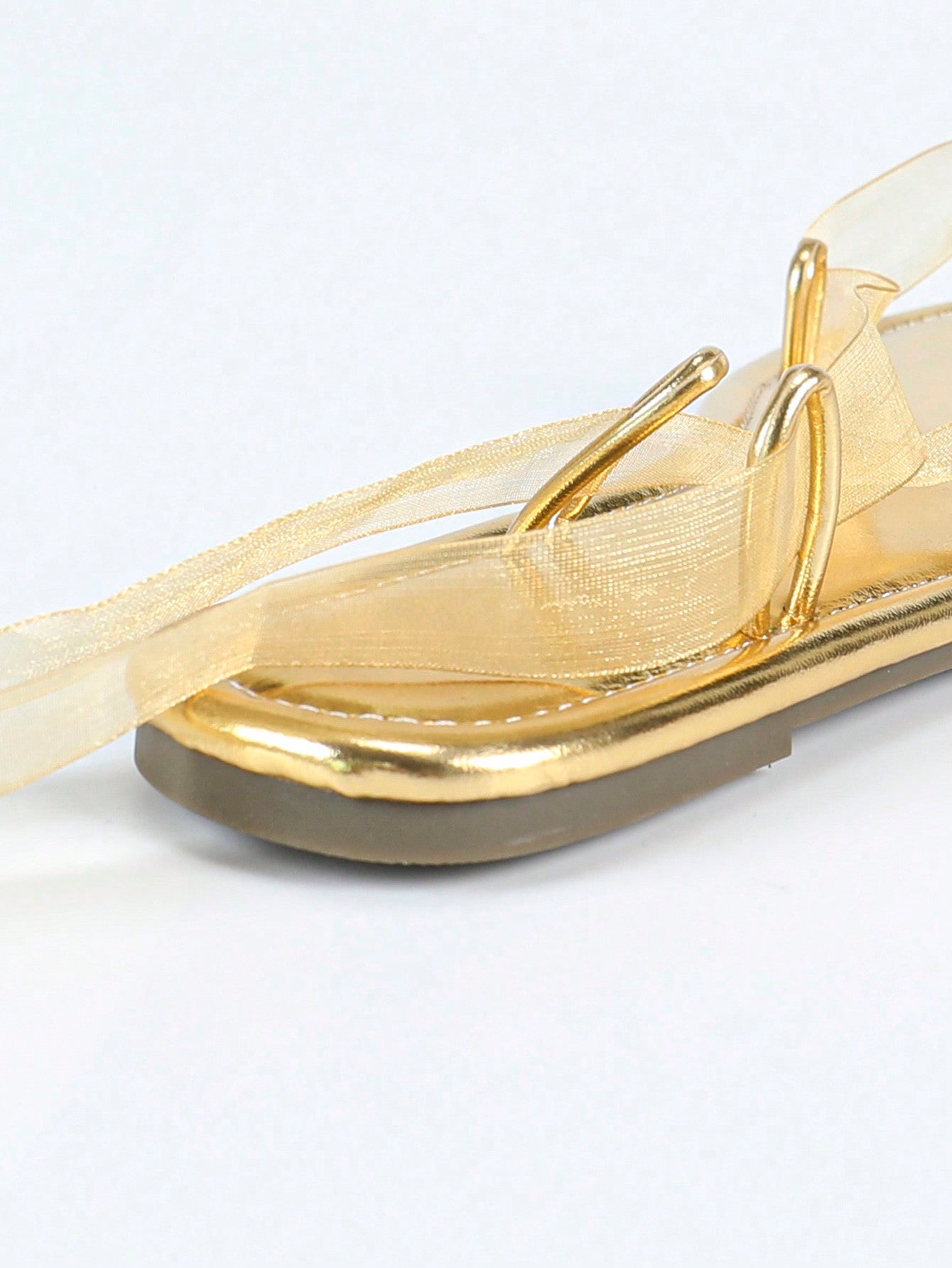 Women's gold flat sandals with metal accent detail, strappy lace-up design, and toe post thong style.