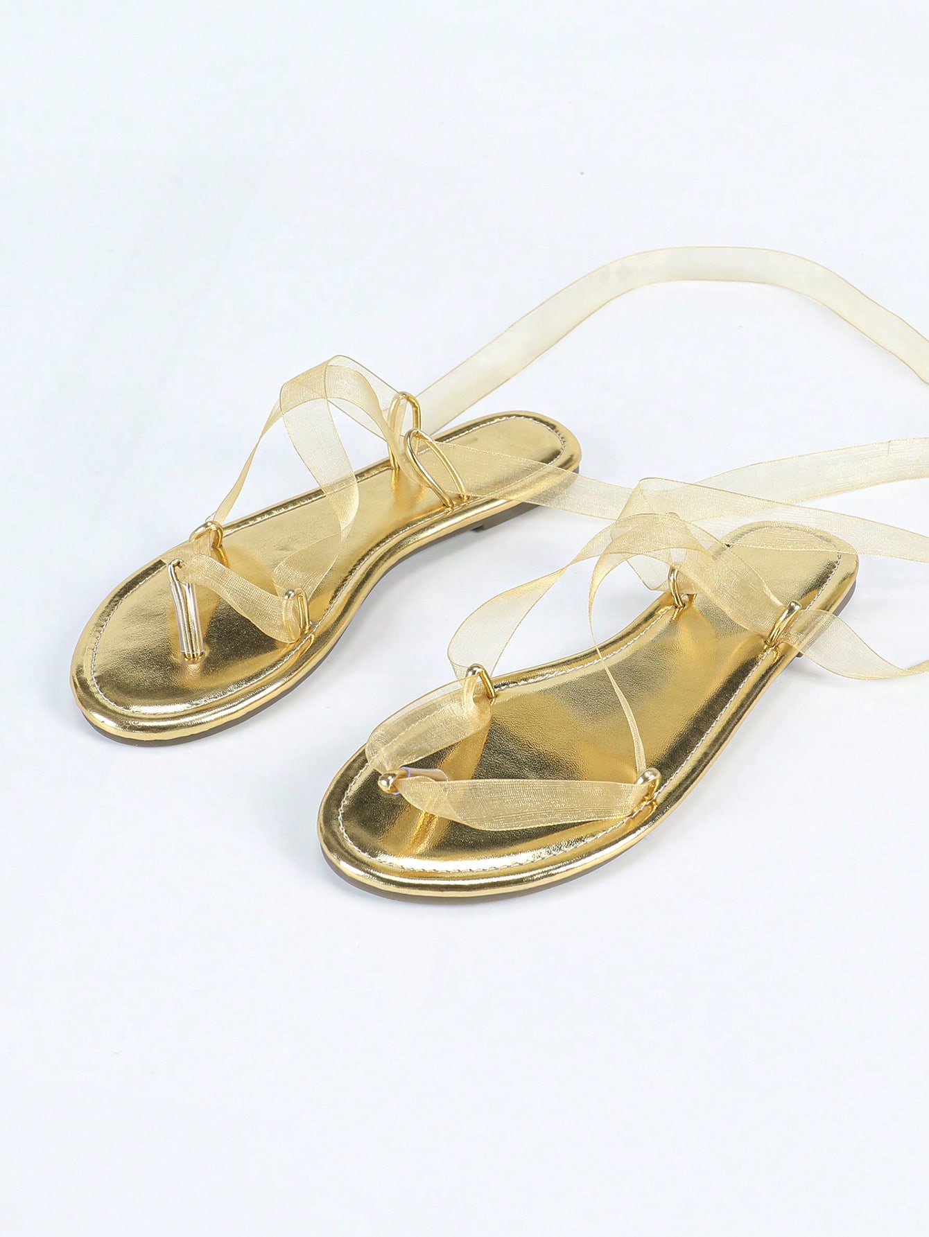 Women's gold flat sandals with metal accent detail, strappy lace-up design, and toe post thong style.