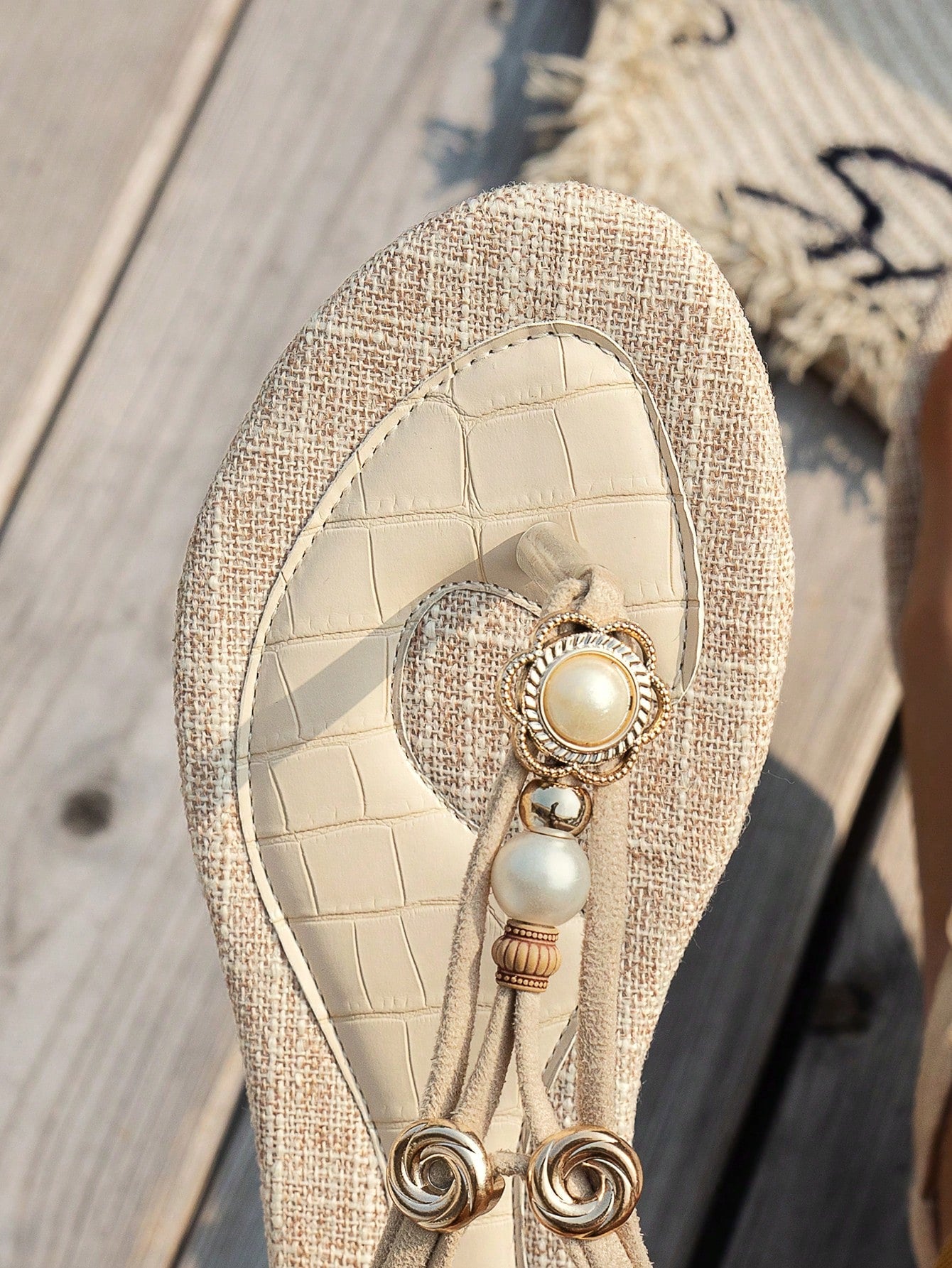 Beige women’s flat thong sandals with braided straps and a woven floral pattern, lightweight beach flip-flop style with toe post and flat sole.