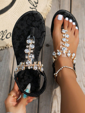 Women's black flat thong sandals with floral print, toe post design, buckle detail, and rhinestone embellishment