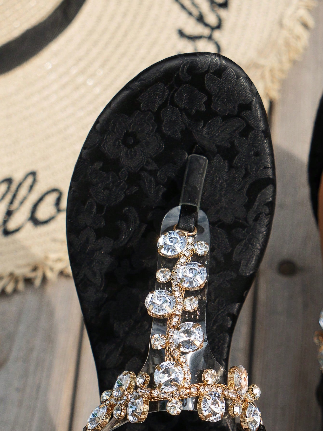 Women's black flat thong sandals with floral print, toe post design, buckle detail, and rhinestone embellishment