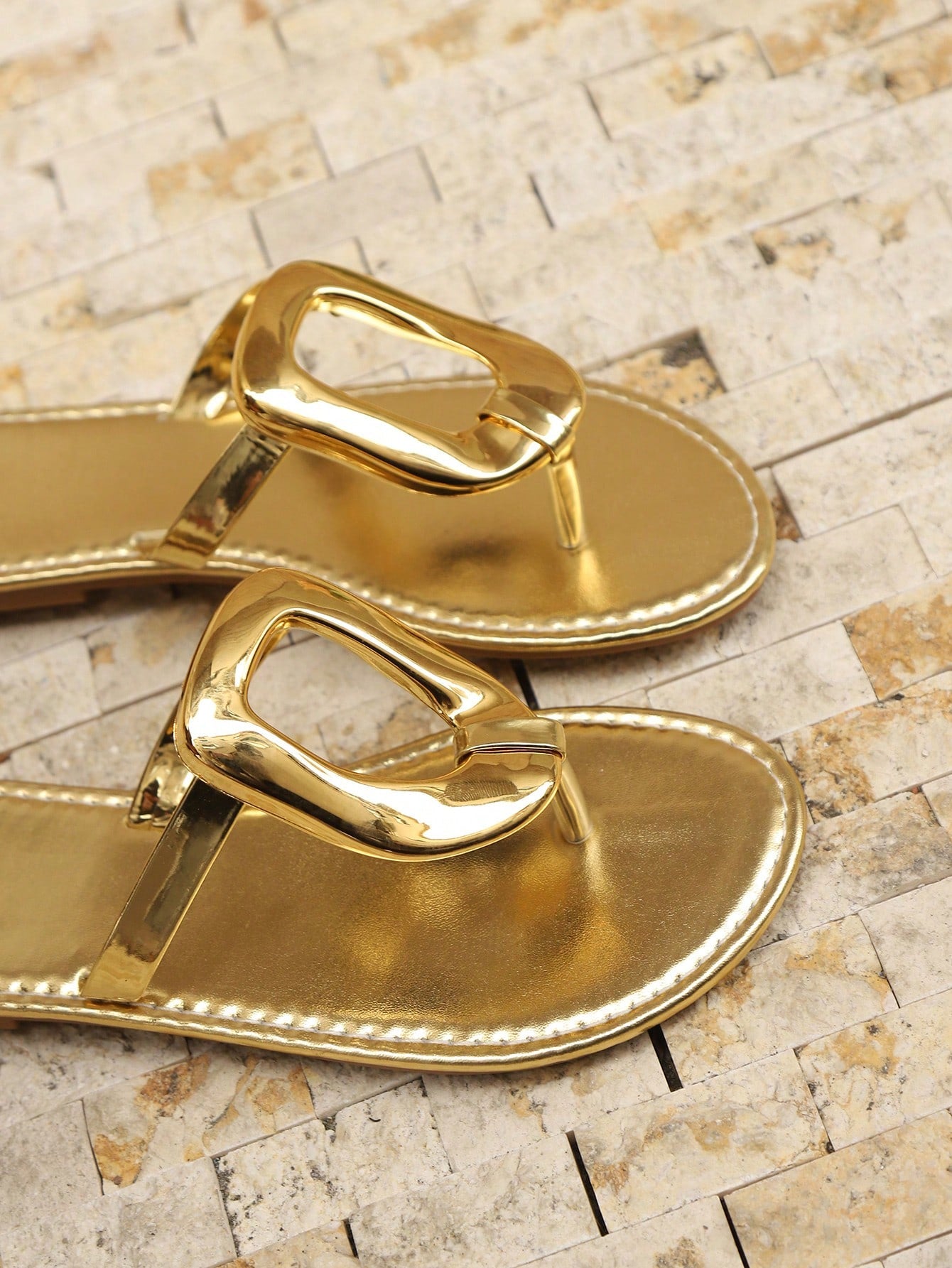 Women’s gold flat slide sandals with open toe post design and metal buckle detail, shown as fashionable outdoor summer footwear.