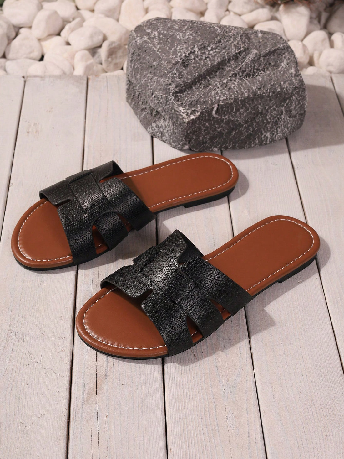 Pair of women's black flat slide sandals with open toes and cut-out detailing in a beach style.