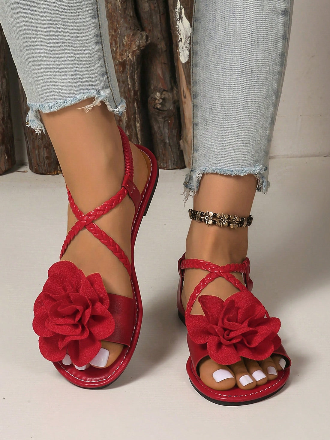 Women's open-toe flat slide sandals with crossed woven-look straps, floral appliqué detail, and buckle accent, shown in a casual beach style.