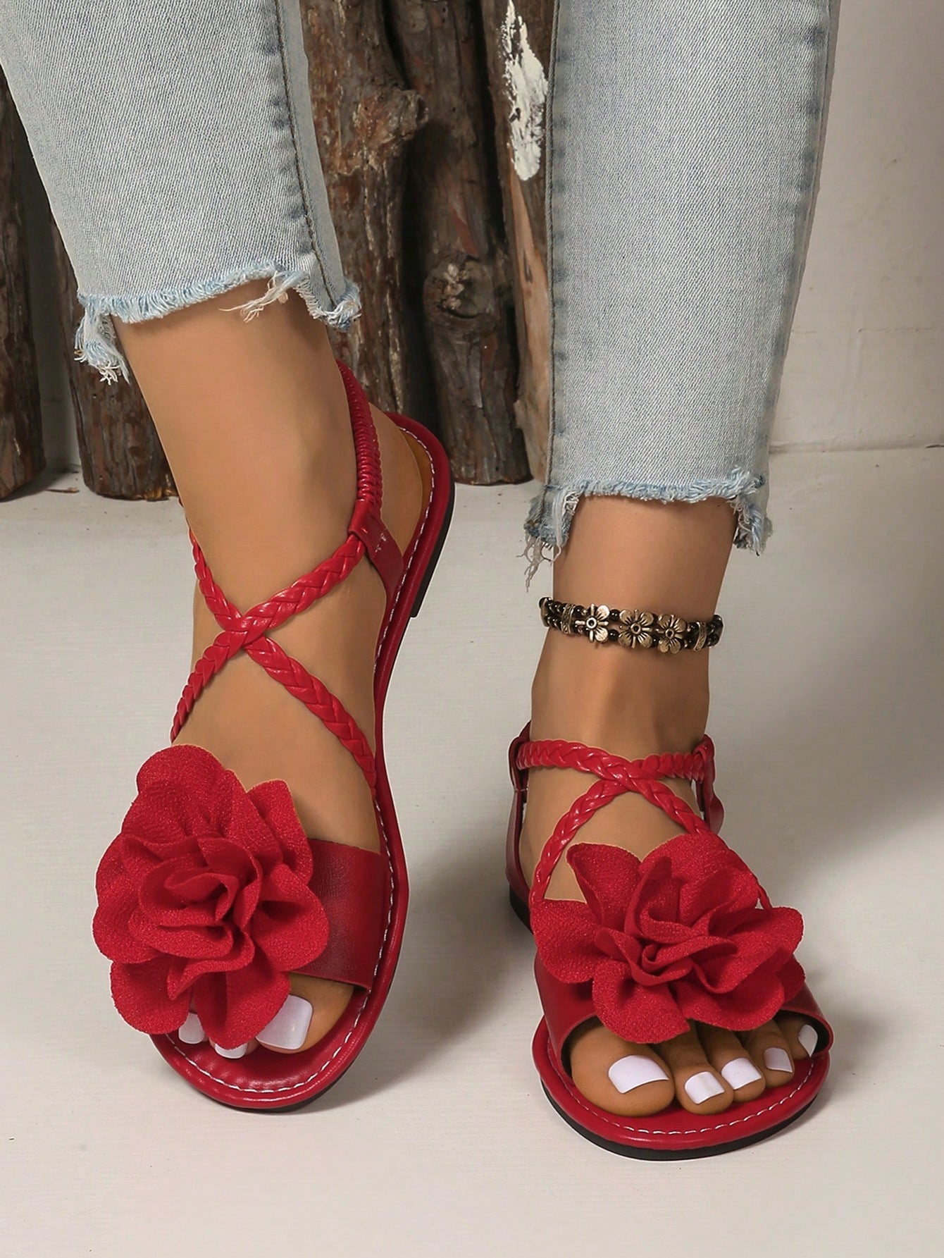 Women's open-toe flat slide sandals with crossed woven-look straps, floral appliqué detail, and buckle accent, shown in a casual beach style.