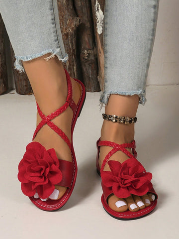 Women's open-toe flat slide sandals with crossed woven-look straps, floral appliqué detail, and buckle accent, shown in a casual beach style.