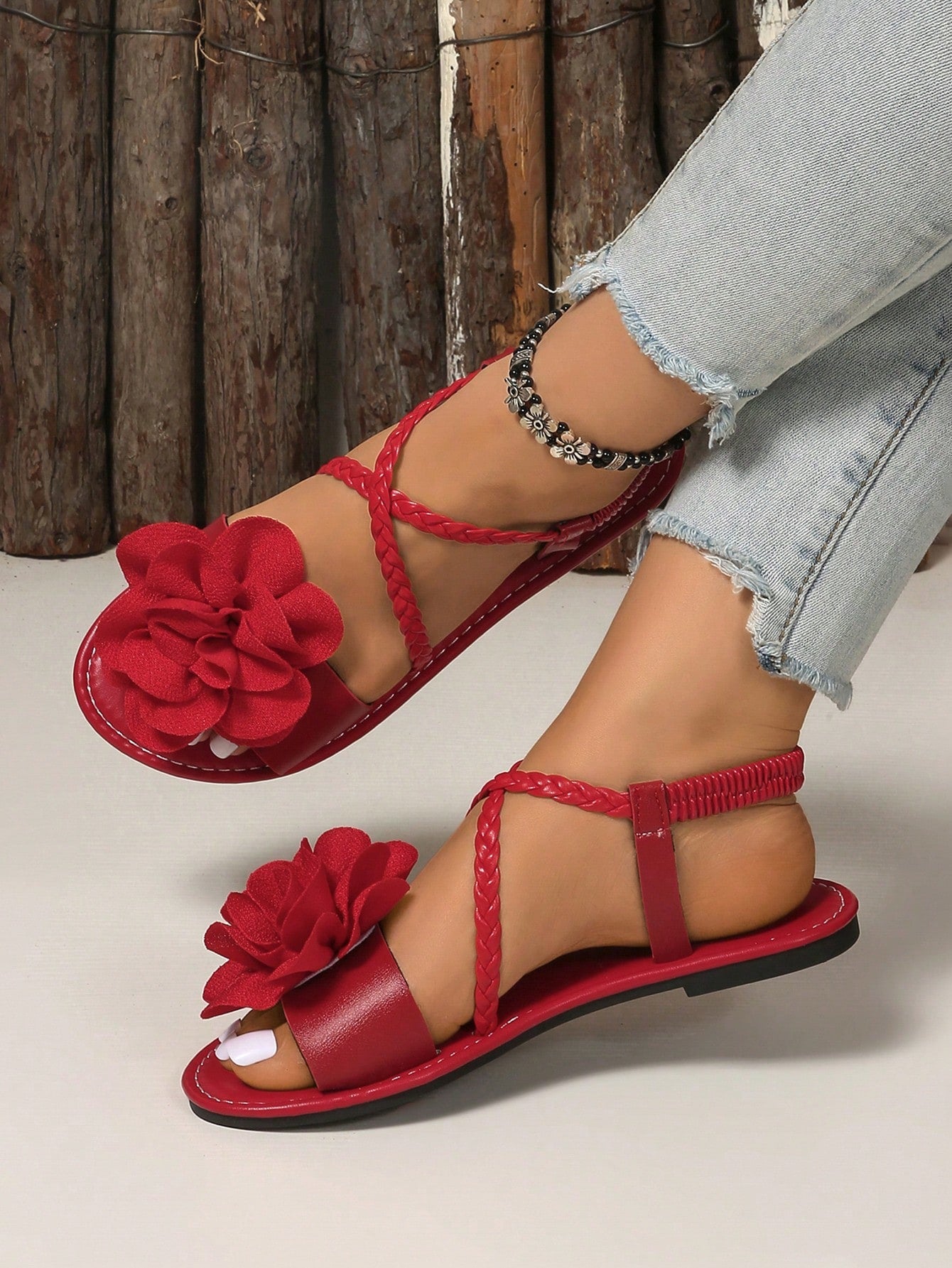 Women's open-toe flat slide sandals with crossed woven-look straps, floral appliqué detail, and buckle accent, shown in a casual beach style.