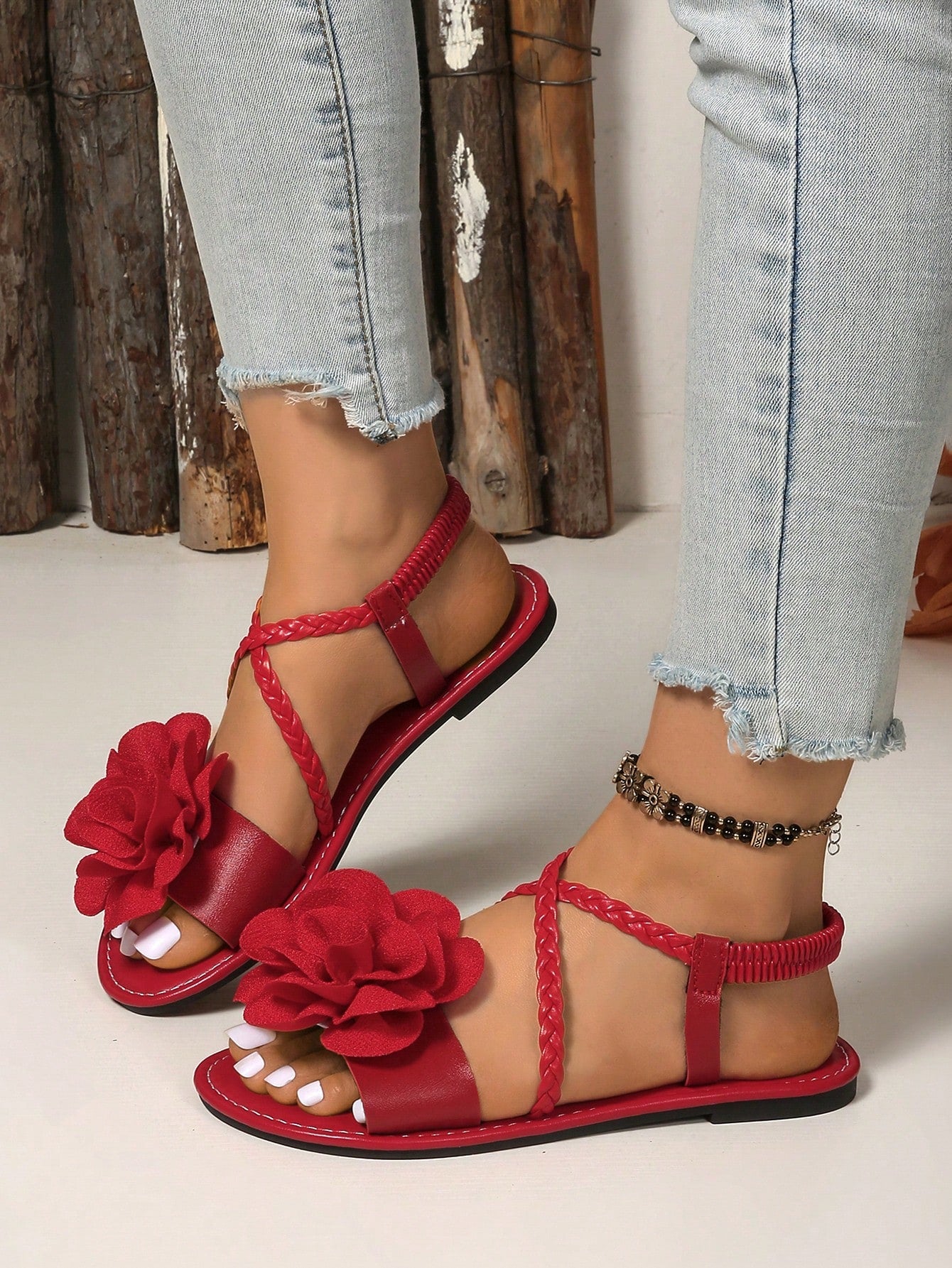Women's open-toe flat slide sandals with crossed woven-look straps, floral appliqué detail, and buckle accent, shown in a casual beach style.