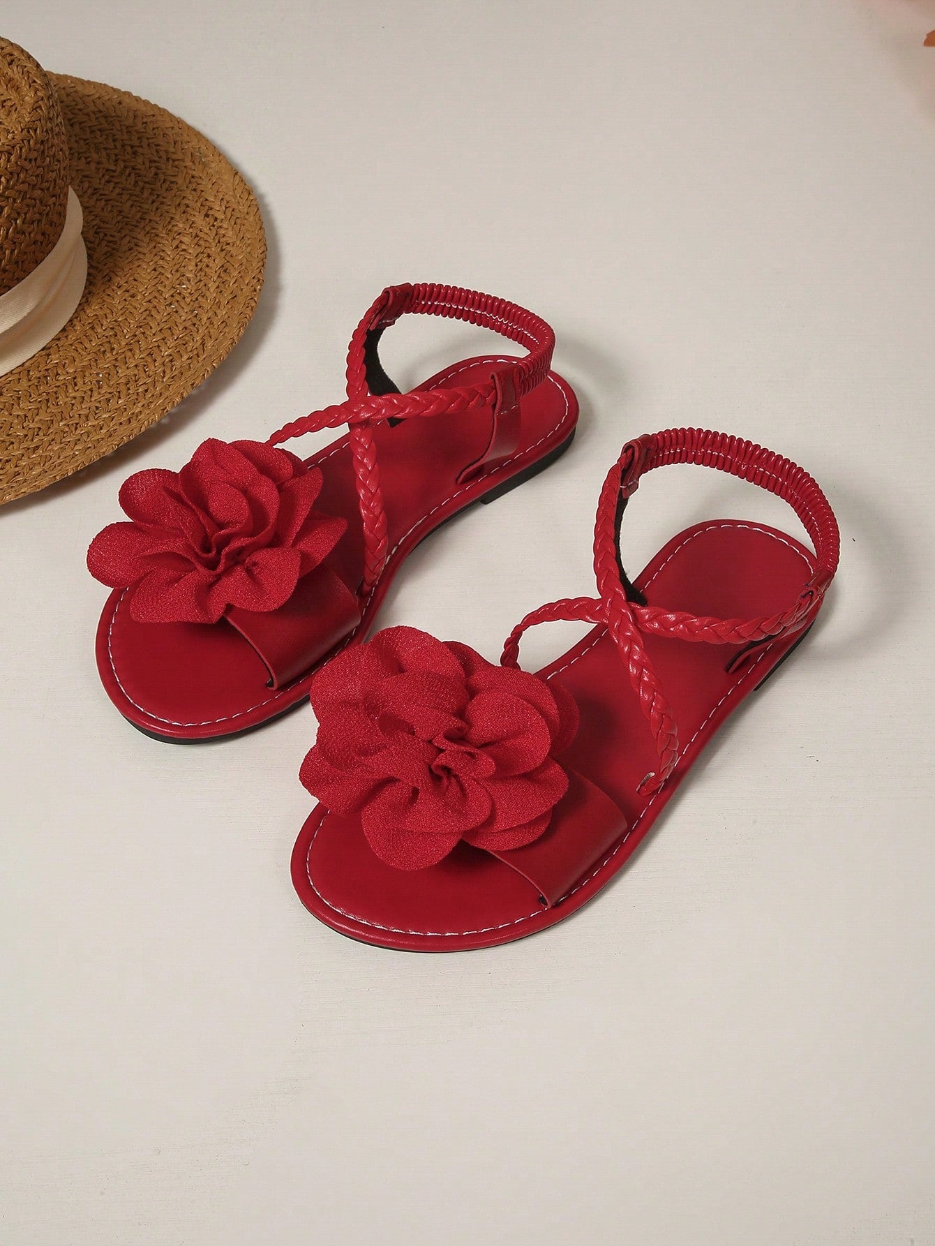 Women's open-toe flat slide sandals with crossed woven-look straps, floral appliqué detail, and buckle accent, shown in a casual beach style.