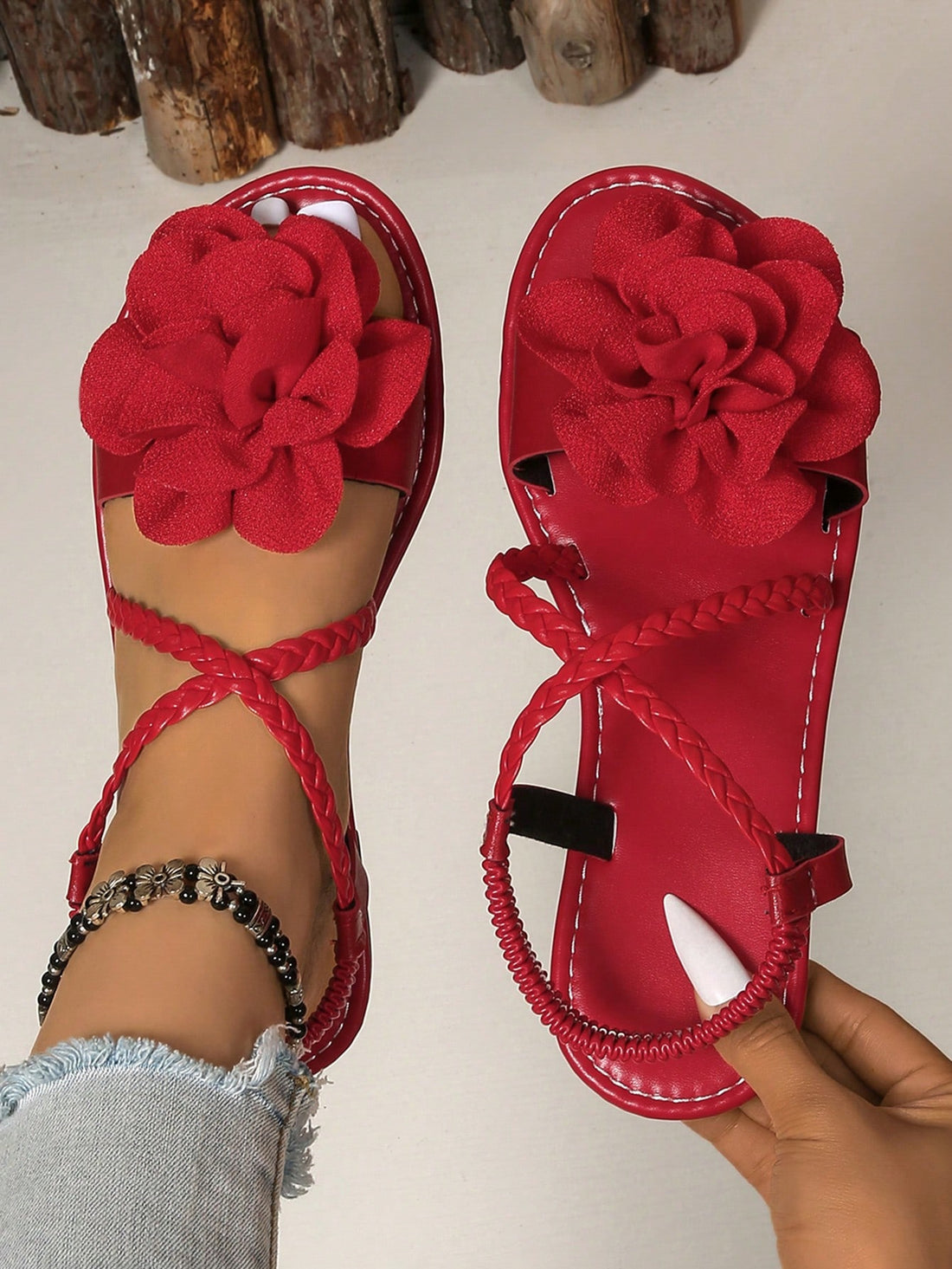 Women's open-toe flat slide sandals with crossed woven-look straps, floral appliqué detail, and buckle accent, shown in a casual beach style.