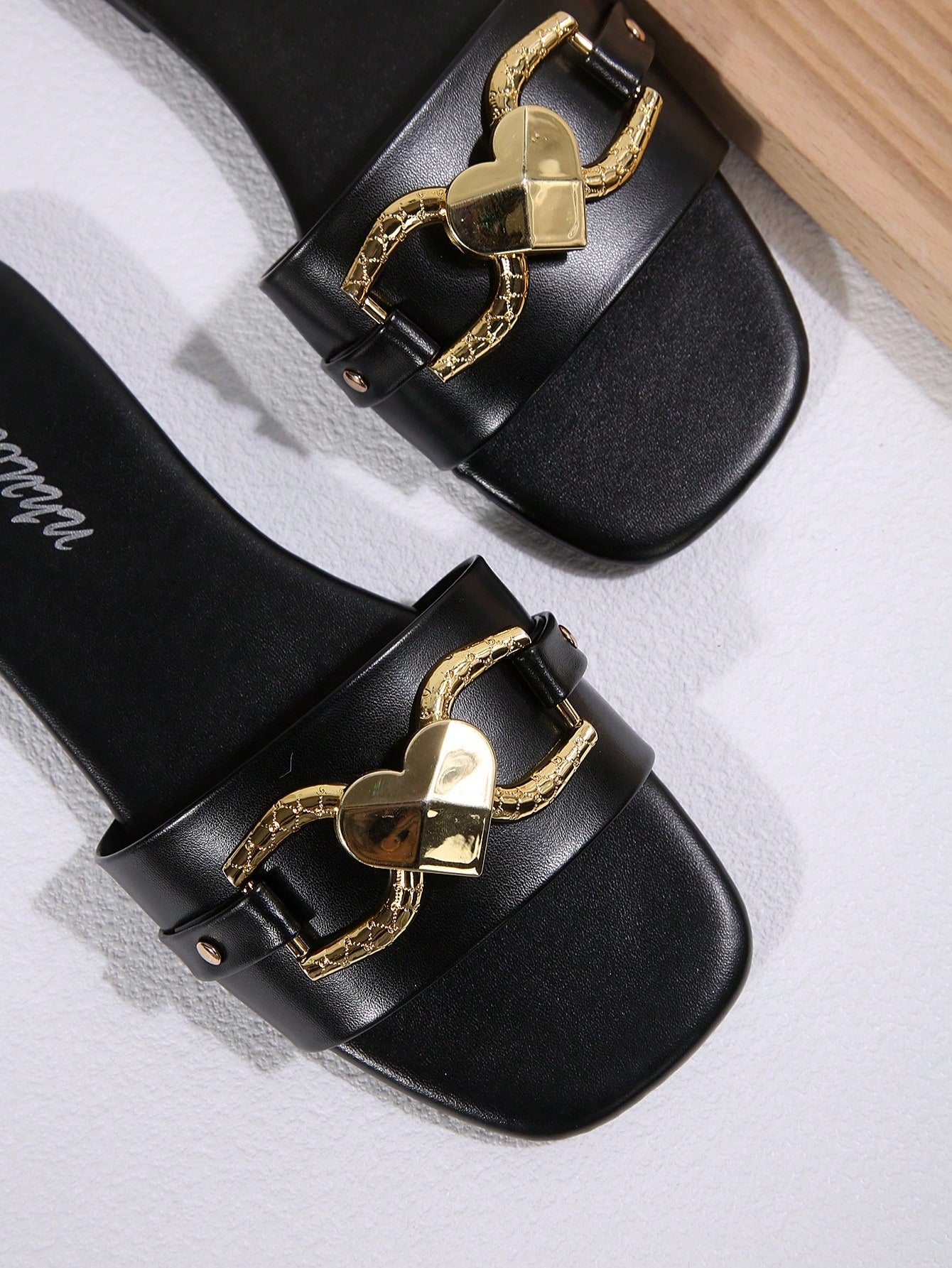 Women's black open-toe slide sandals featuring a 3D heart buckle detail and flat sole, suitable for casual indoor and outdoor summer wear.
