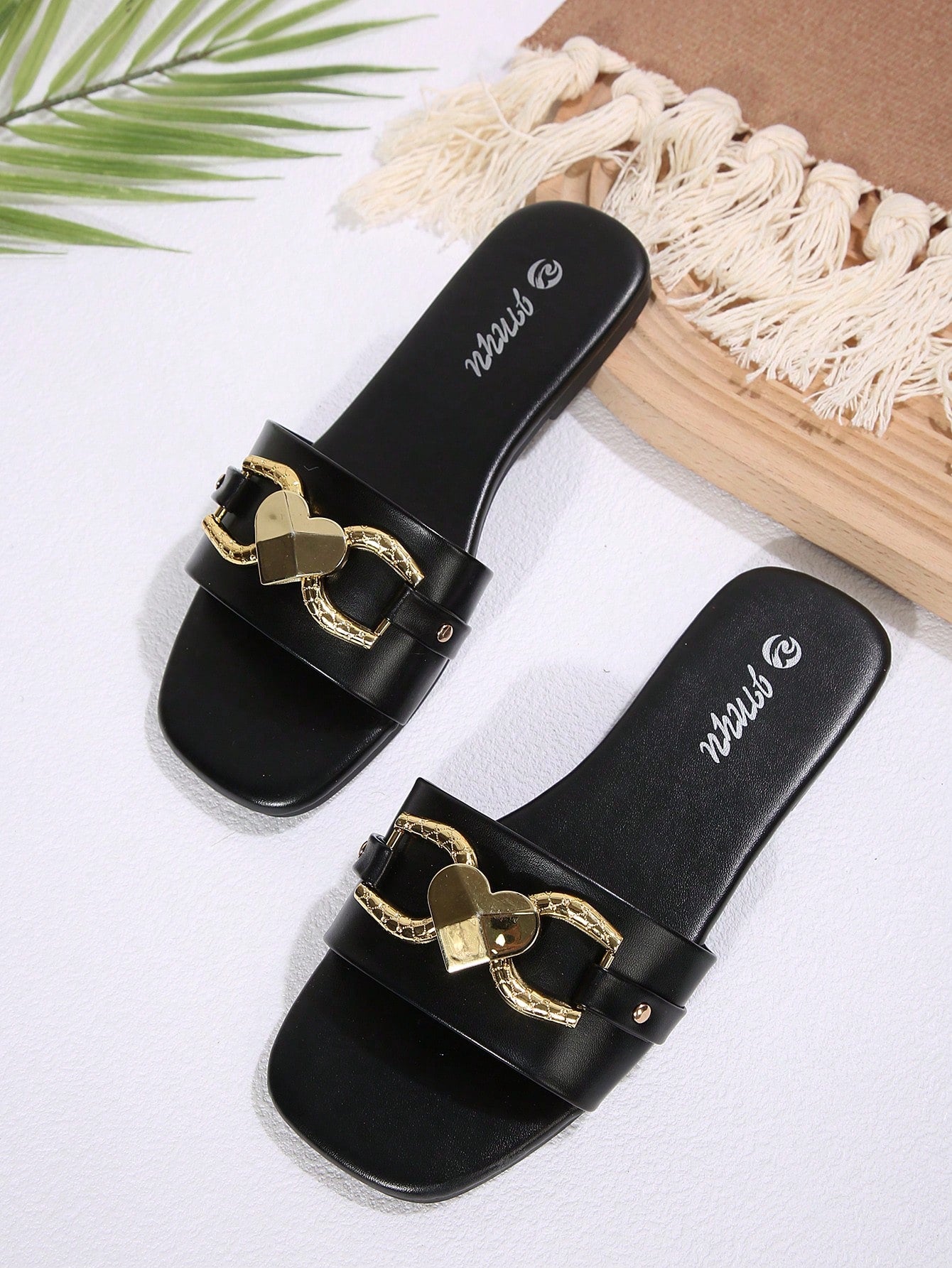 Women's black open-toe slide sandals featuring a 3D heart buckle detail and flat sole, suitable for casual indoor and outdoor summer wear.