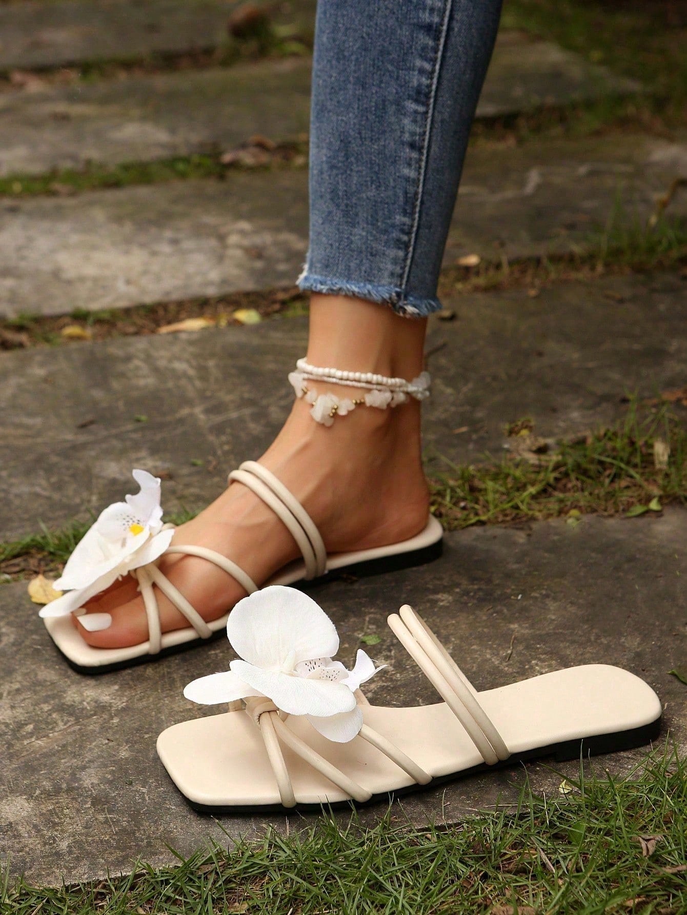 Women's flat slide sandals with open toe, floral applique detail, and criss-cross straps, shown as casual vacation-style summer footwear.