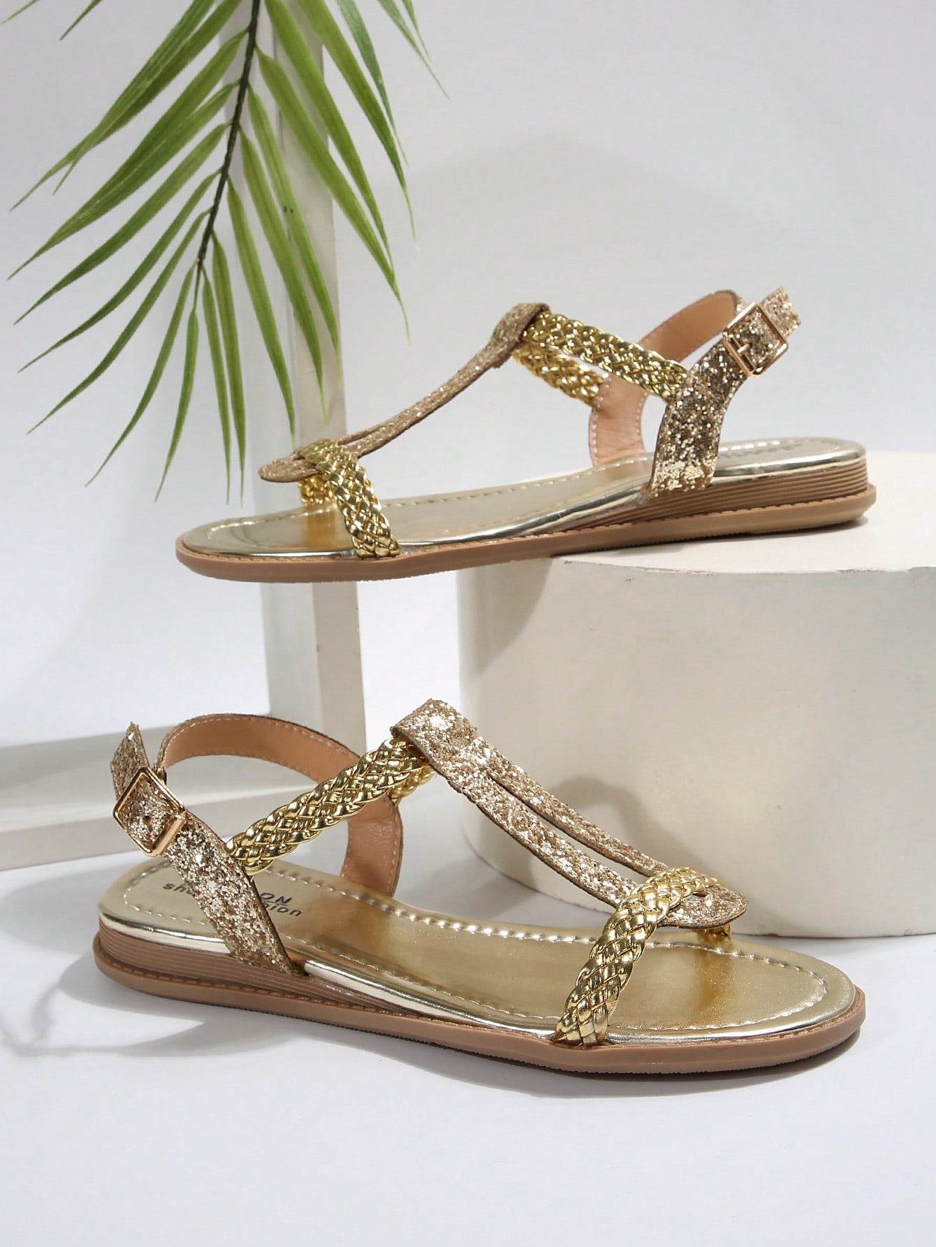 Pair of elegant gold flat gladiator sandals with a shiny woven PU leather design, open toe, and buckle closure.
